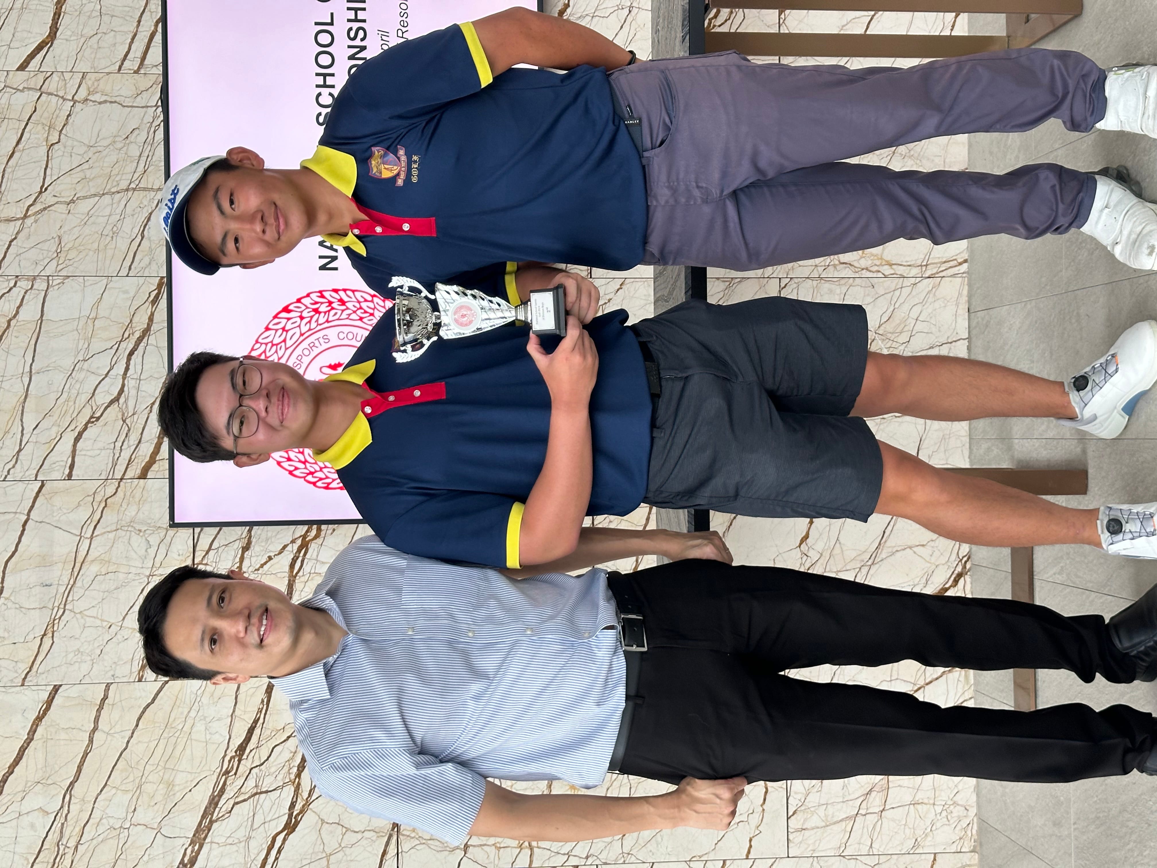 Three men pose together, two in navy golf uniforms holding a silver trophy, at a National School Championship event.
