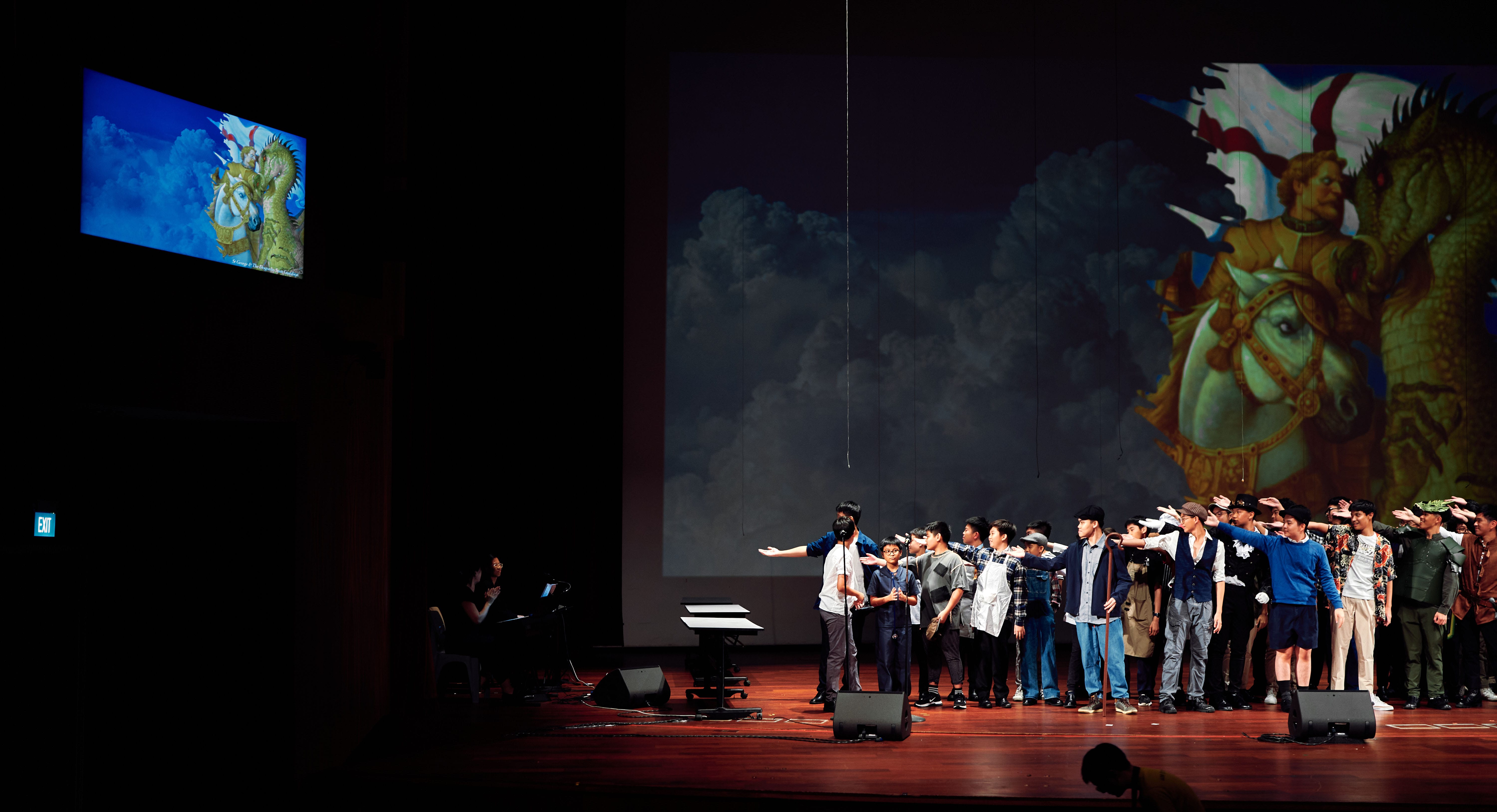 A group of performers on a dark stage with a large projected fantasy knight artwork backdrop behind them.