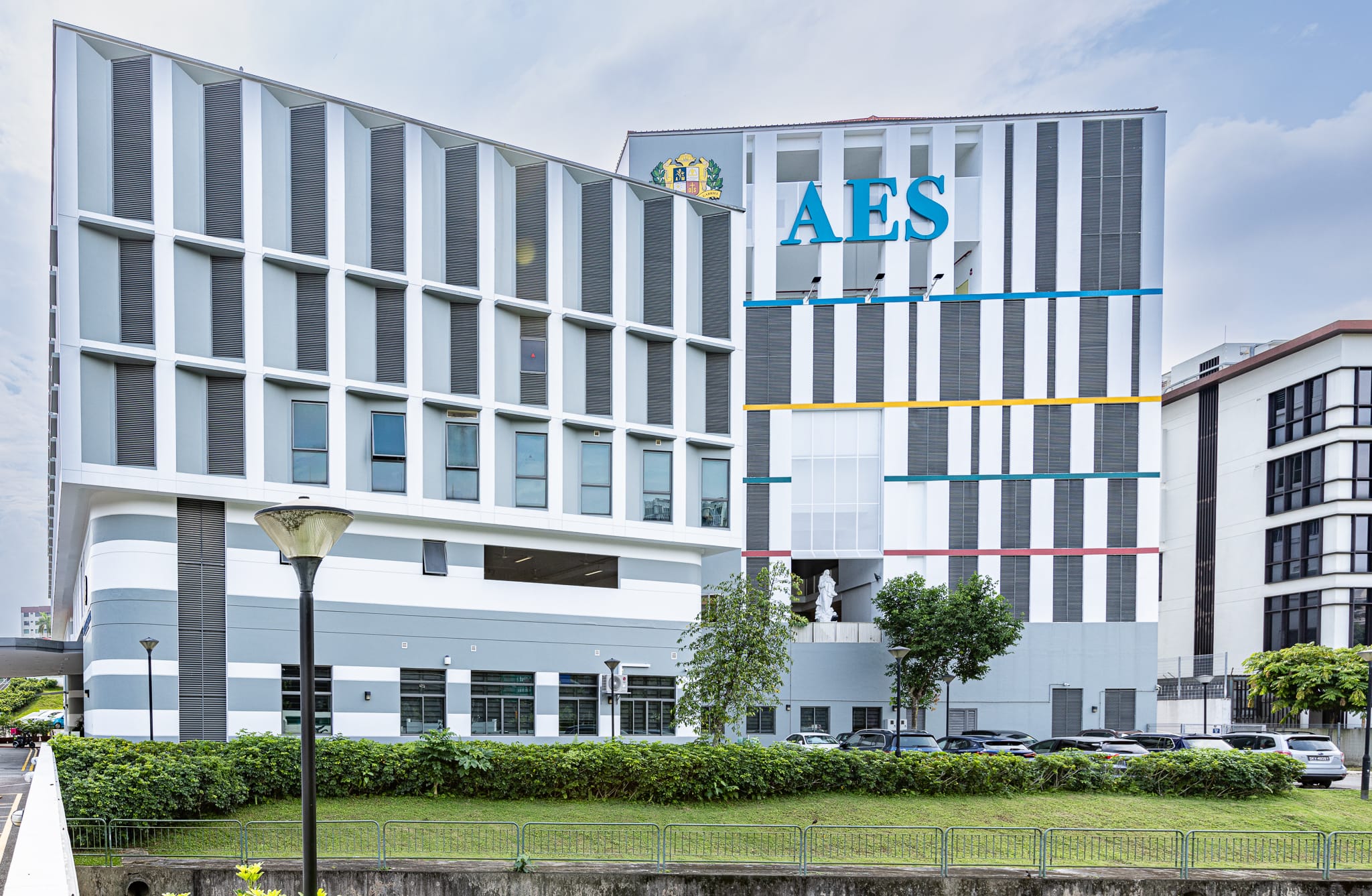 Modern multi-story AES building with white and gray facade, colorful horizontal stripes, and large blue letters on top.