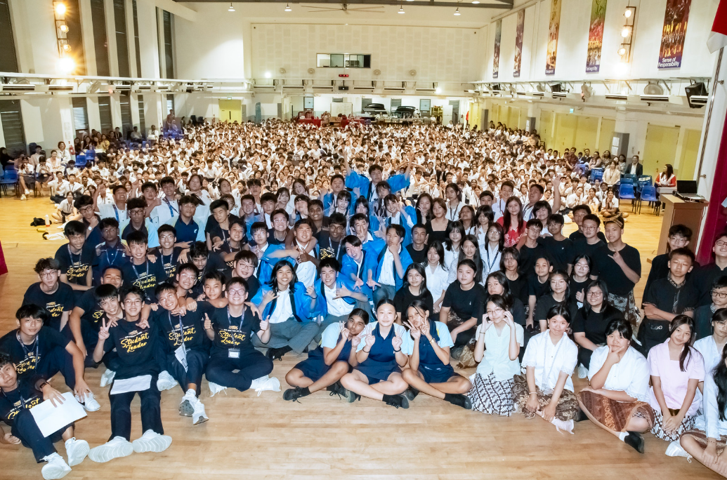 Large group of school students in uniforms posing together in a hall, with some wearing black Student Leader shirts.