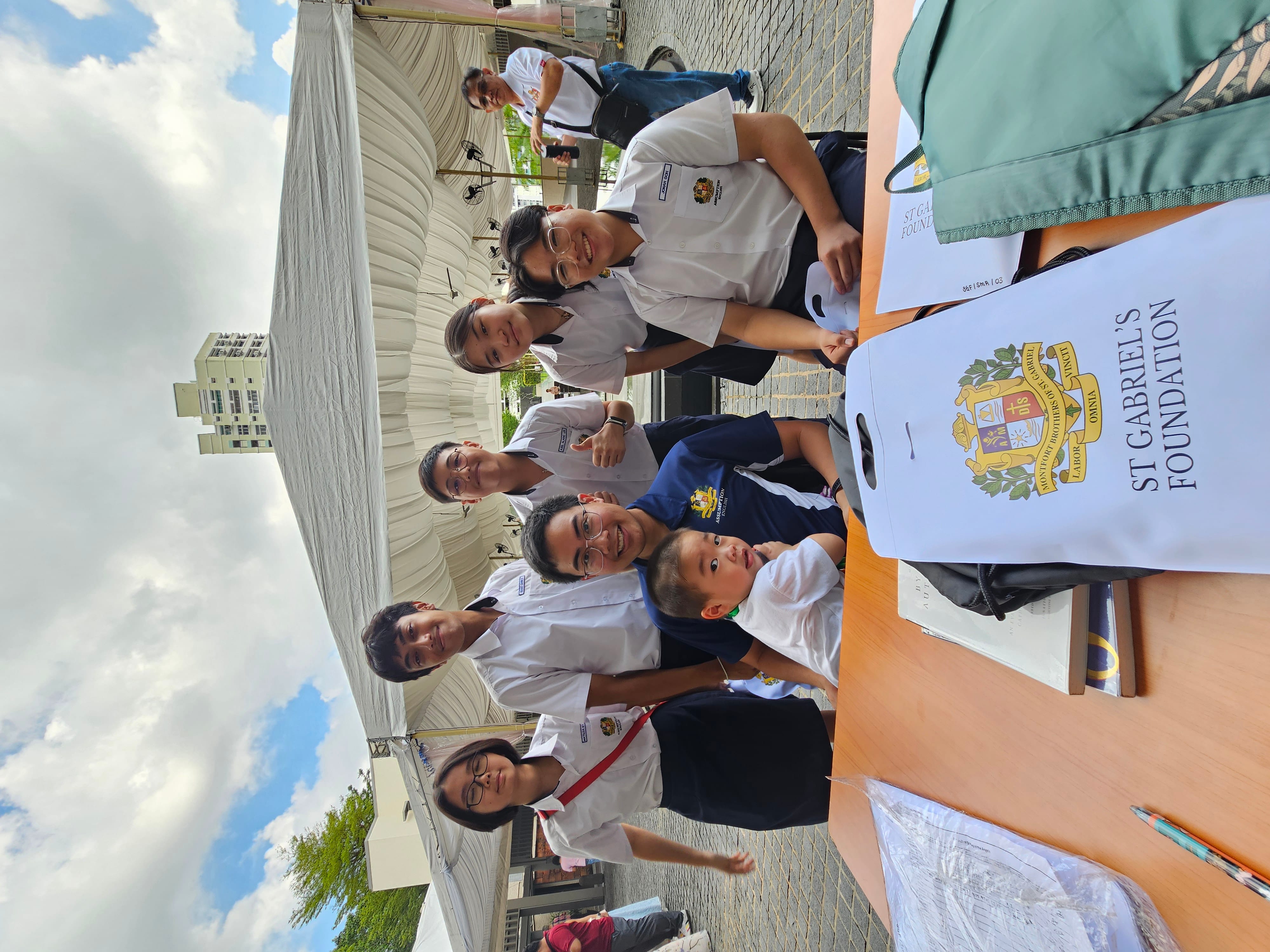 Group of students in school uniforms posing outdoors near a table with a St Gabriel's Foundation bag.