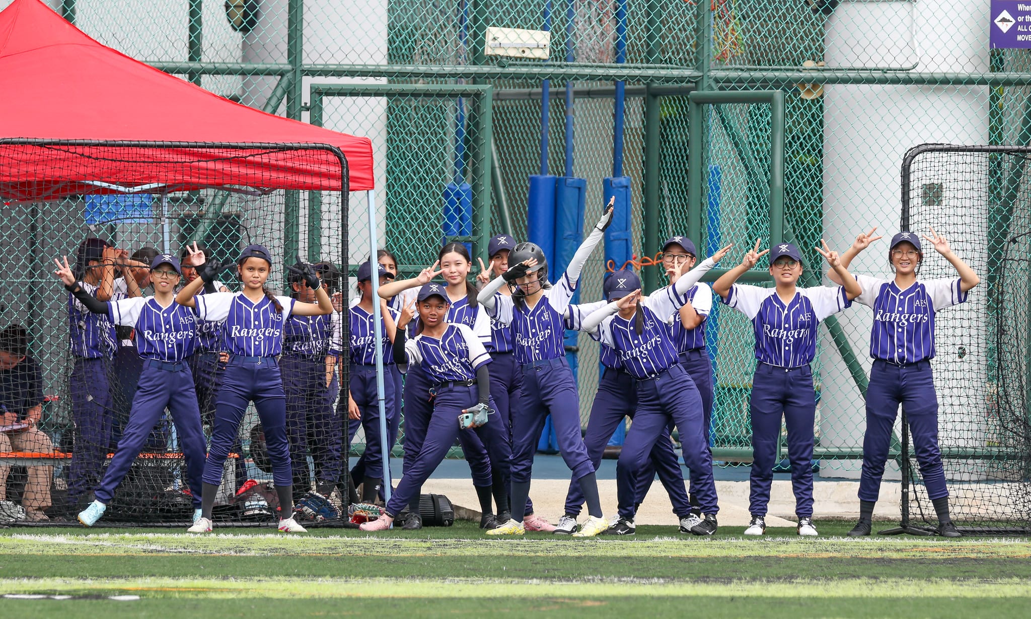 A group of young girls in purple Rangers softball uniforms posing with peace signs on a field.