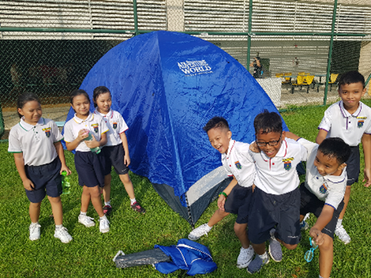Seven children in school uniforms gather around a small blue dome tent on a grass field.