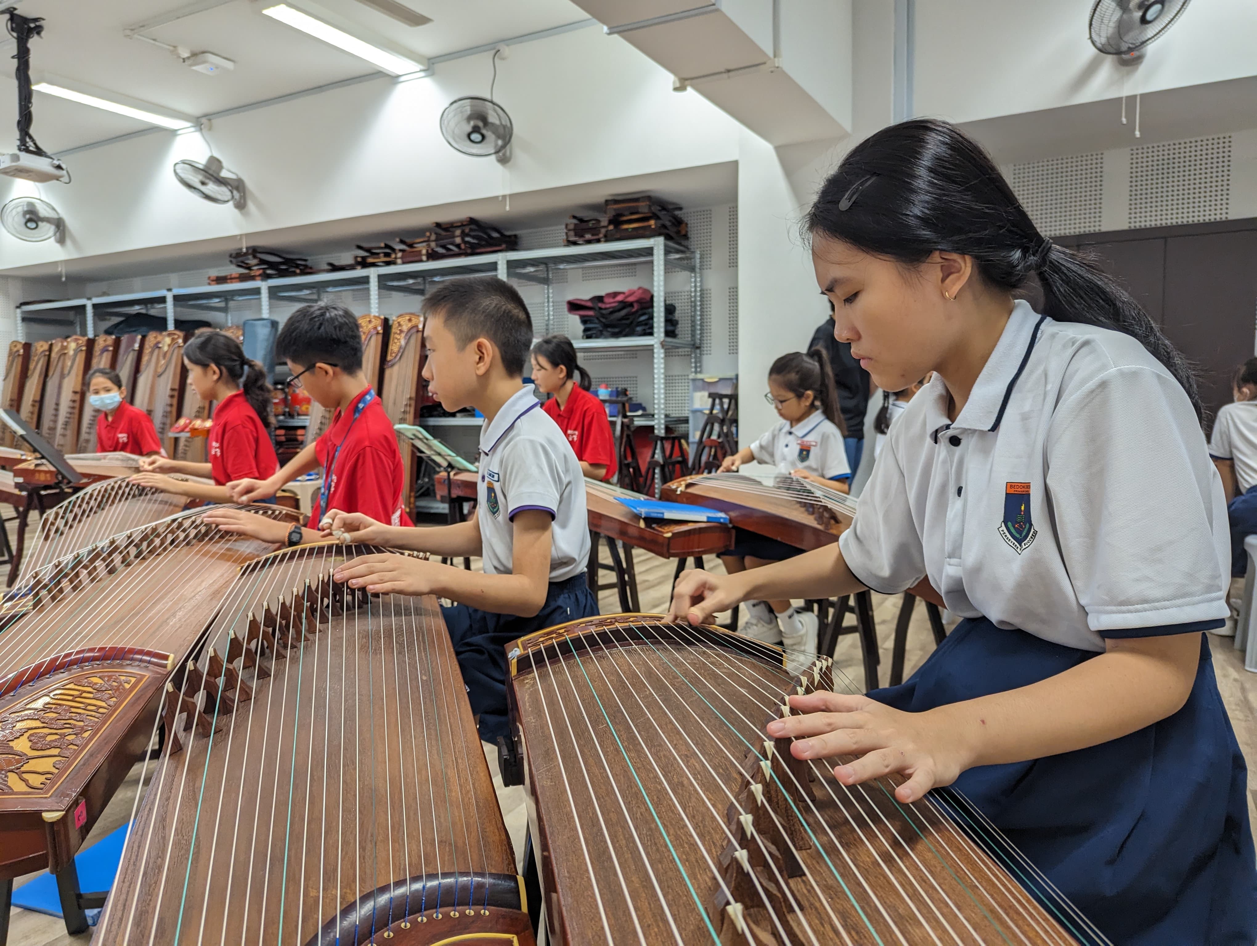 Students in school uniforms practice playing guzheng instruments in a classroom setting.