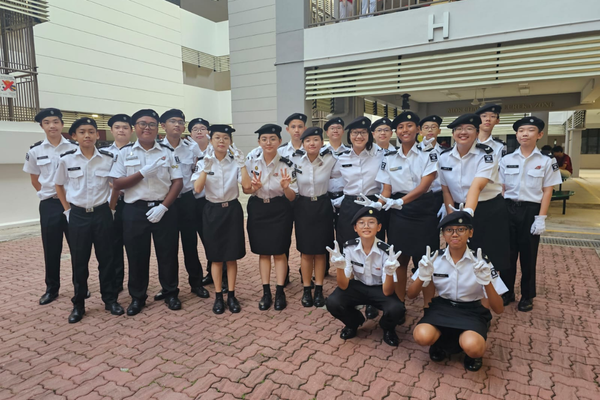 A group of young people in matching white and black uniforms with black berets posing together outdoors.