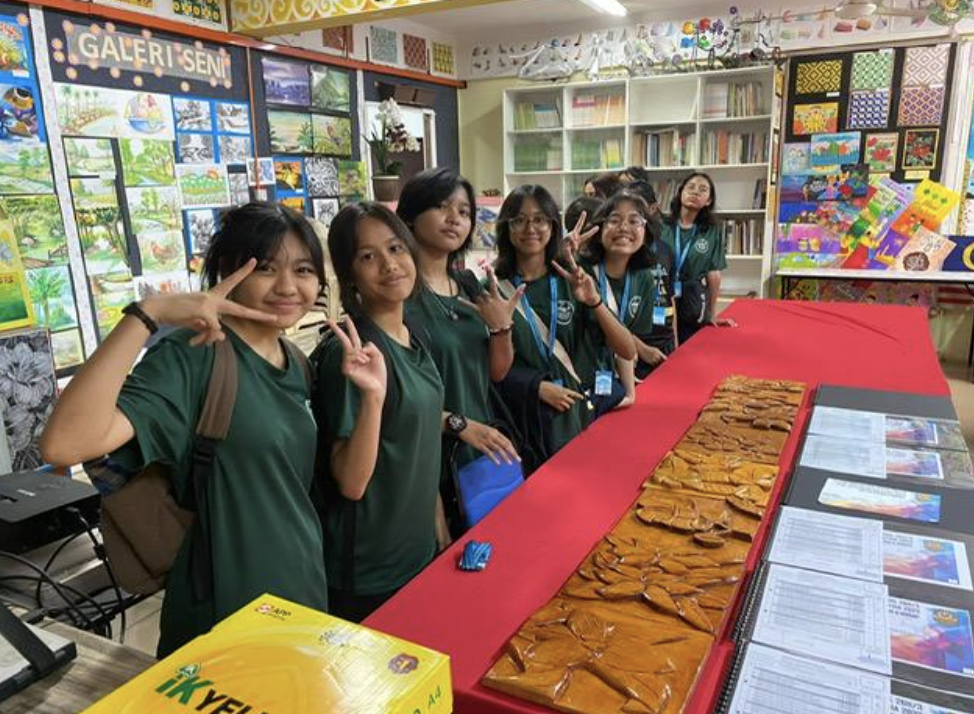 Students in green uniforms pose with peace signs in a colorful art gallery room labeled Galeri Seni.