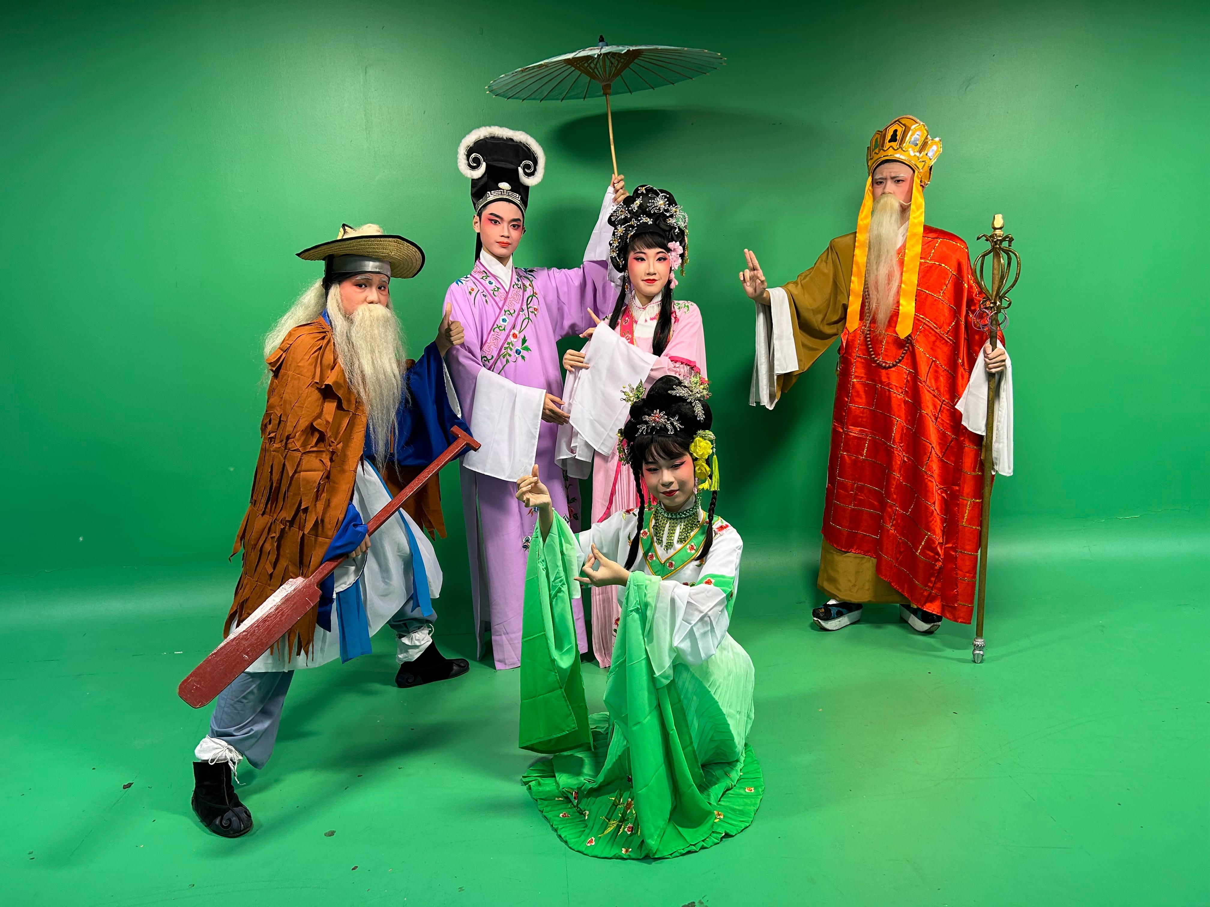 Five performers in traditional Chinese opera costumes and makeup pose before a green screen backdrop.