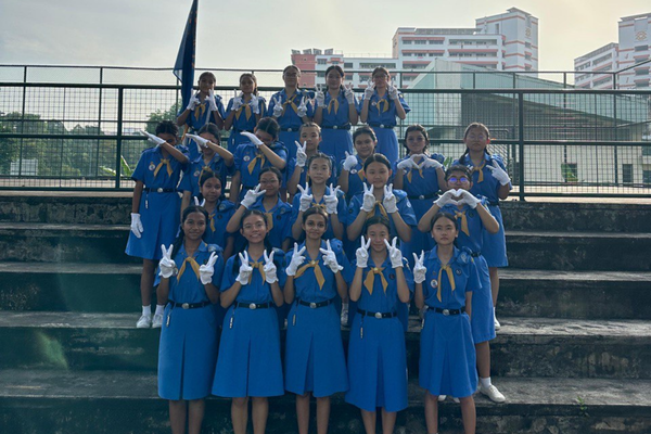 A group of girls in blue uniforms and white gloves pose on outdoor steps making hand gestures.