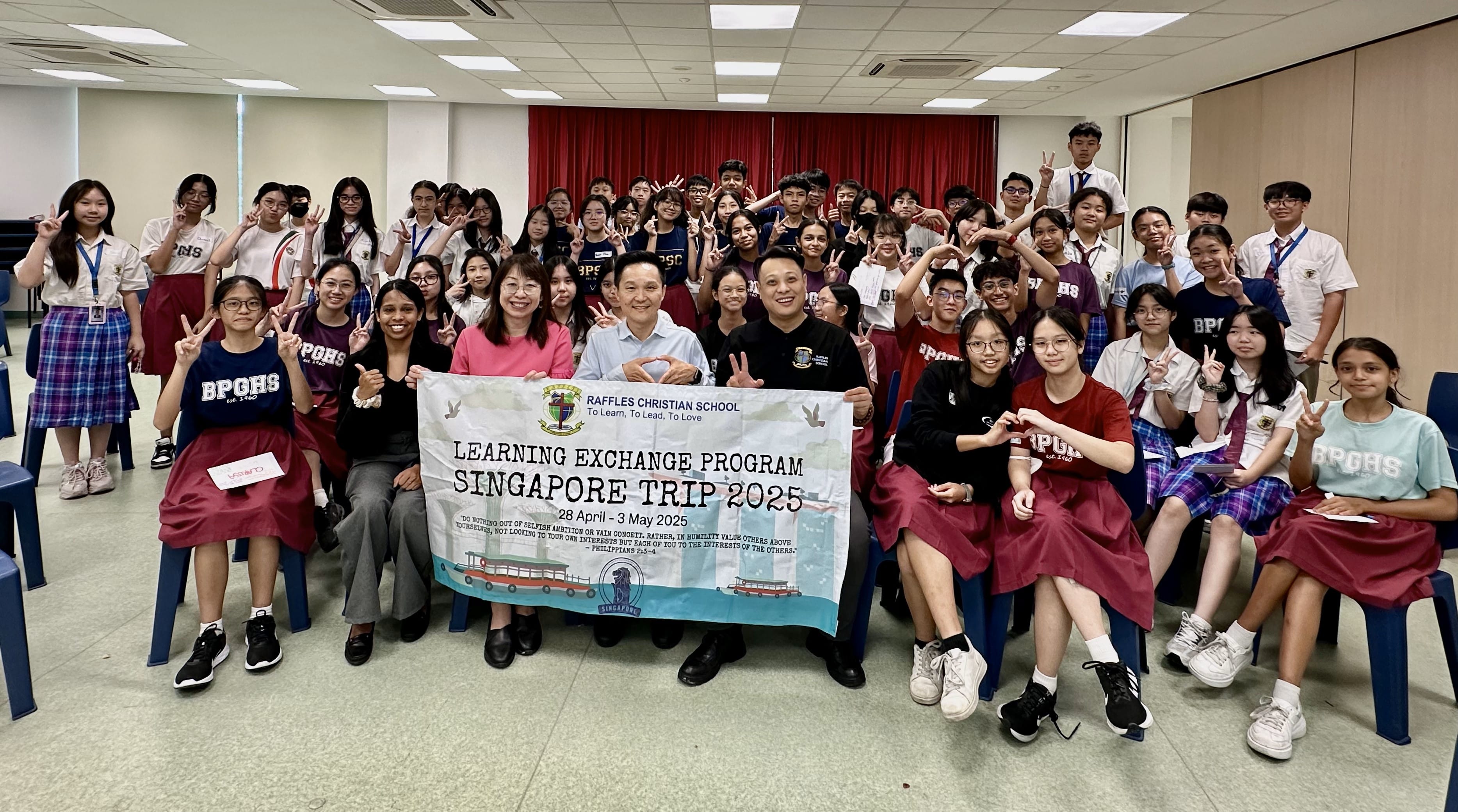 Large group of students and teachers posing with a Raffles Christian School Singapore Trip 2025 banner.