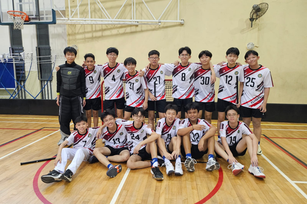 A youth floorball team poses in two rows on an indoor court wearing white and red numbered jerseys.