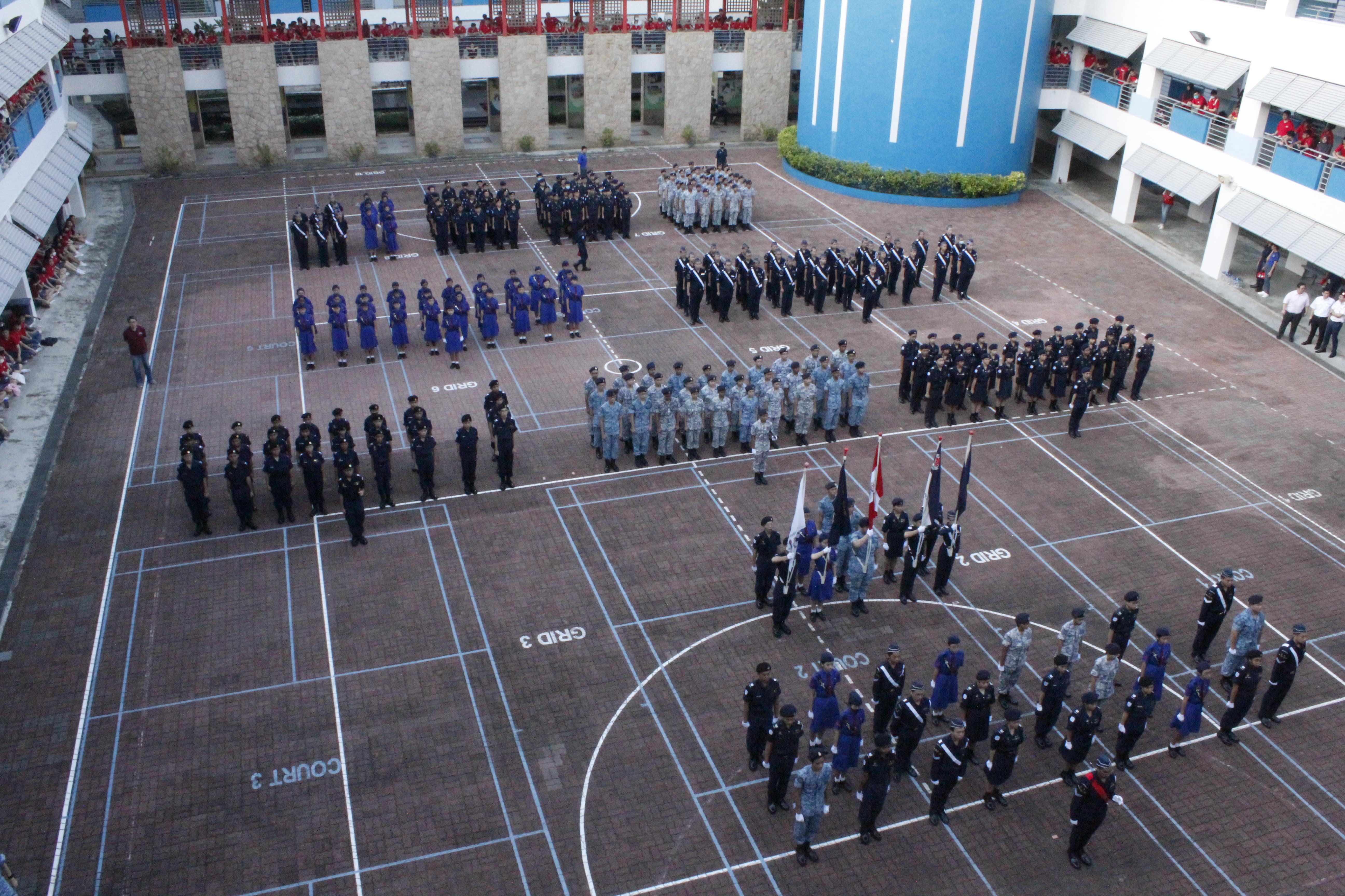 Aerial view of uniformed cadets standing in formation on a school courtyard during a parade ceremony.