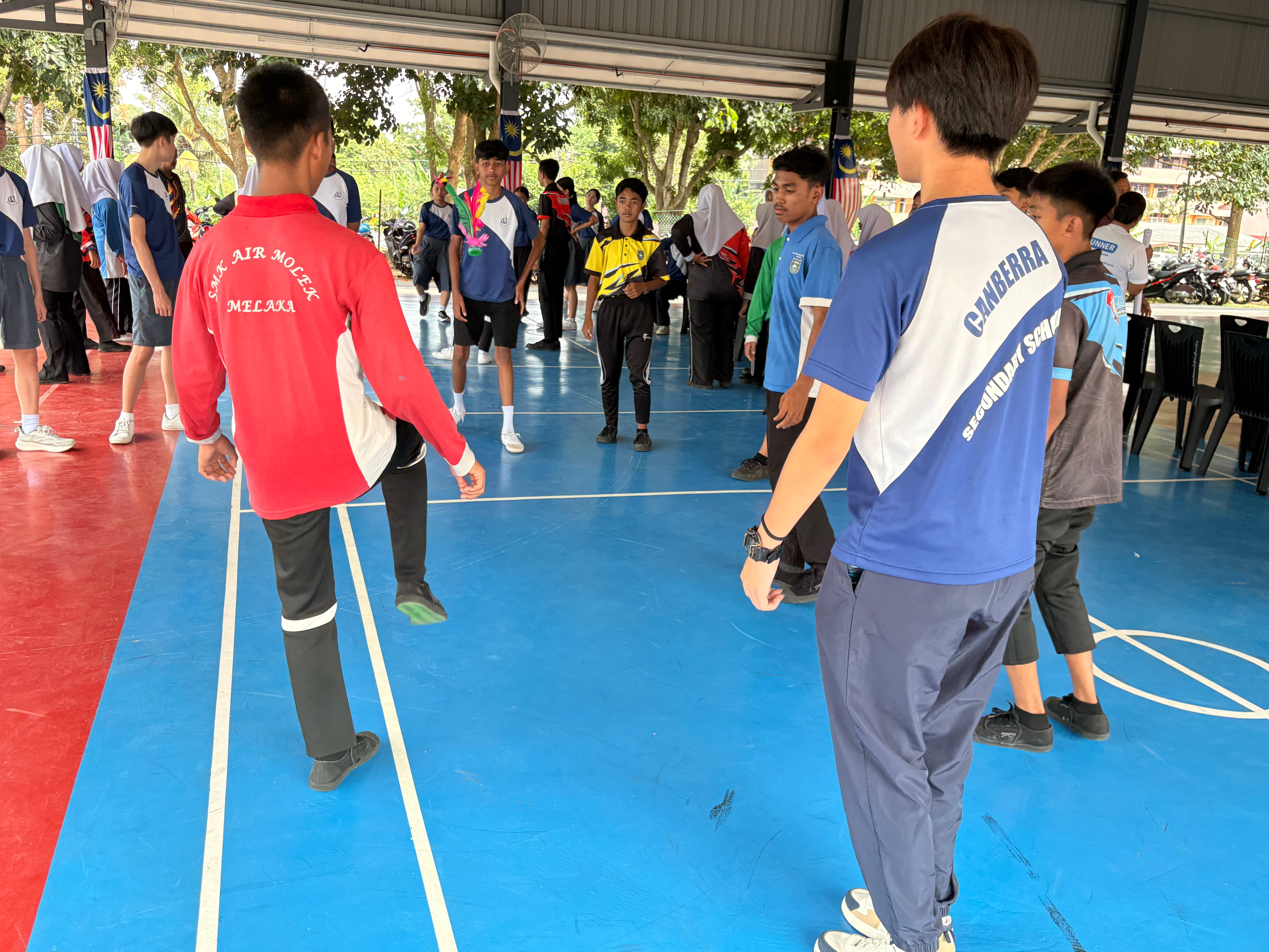 Students stand in a circle on a covered court, with one in red stepping forward and others watching.