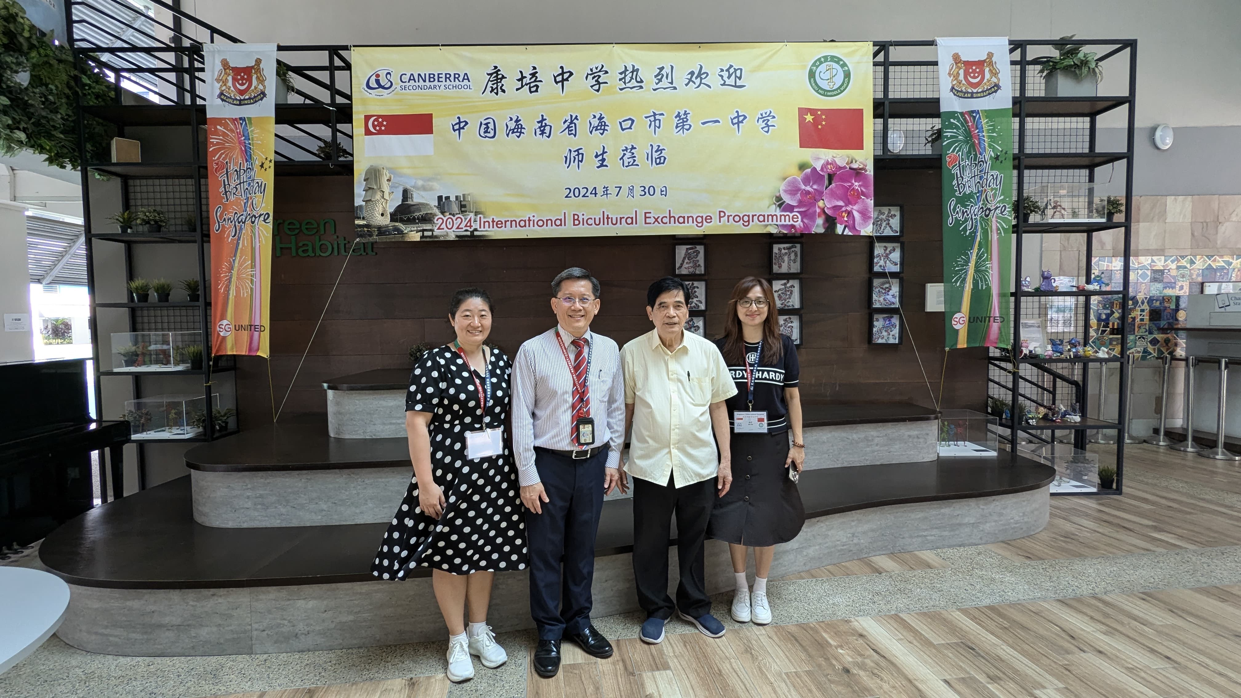 Four people stand before a banner for the 2024 International Bicultural Exchange Programme at Canberra Secondary School.
