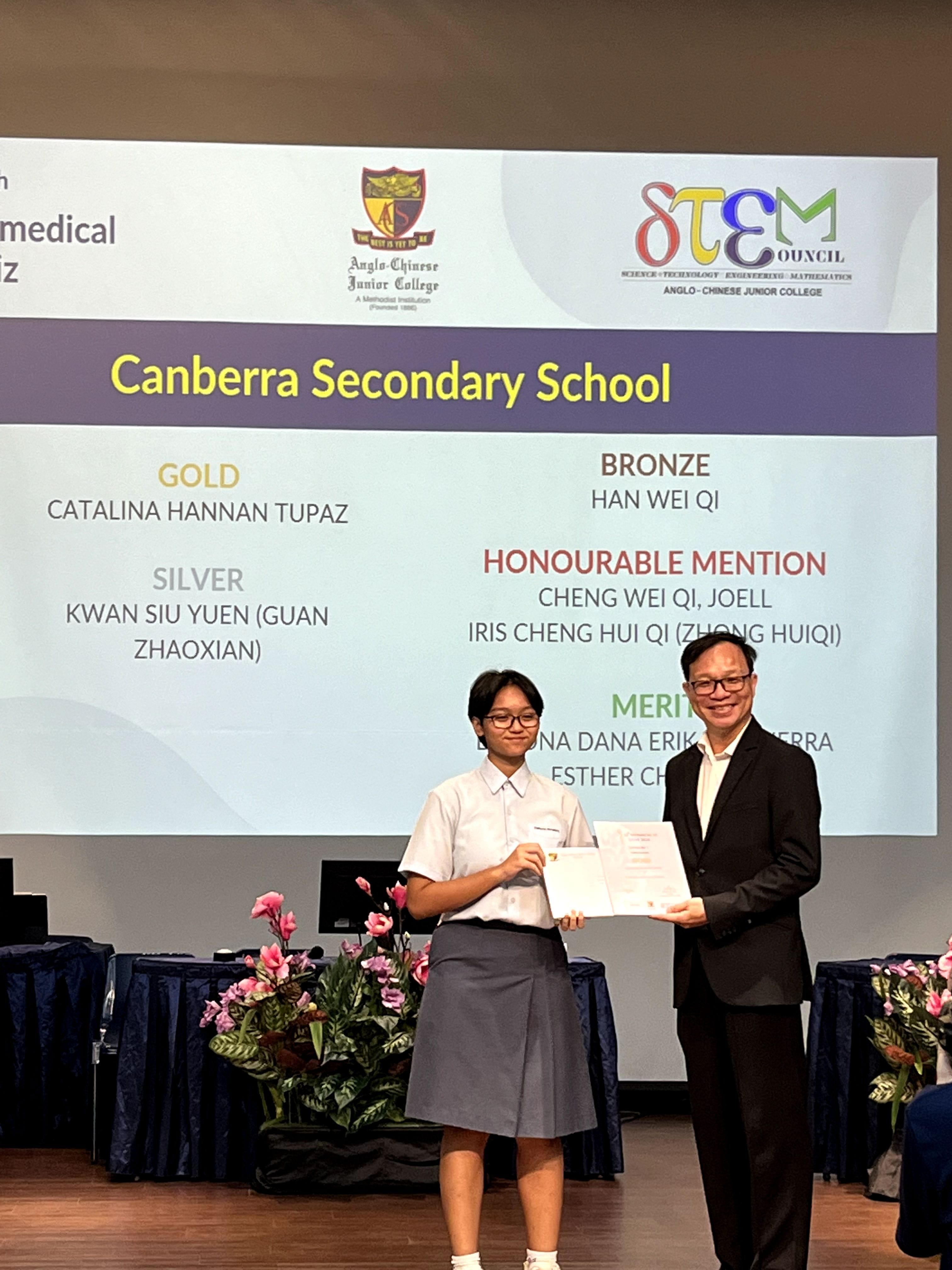 A student in school uniform receives a certificate from a man in a suit in front of a Canberra Secondary School awards slide.