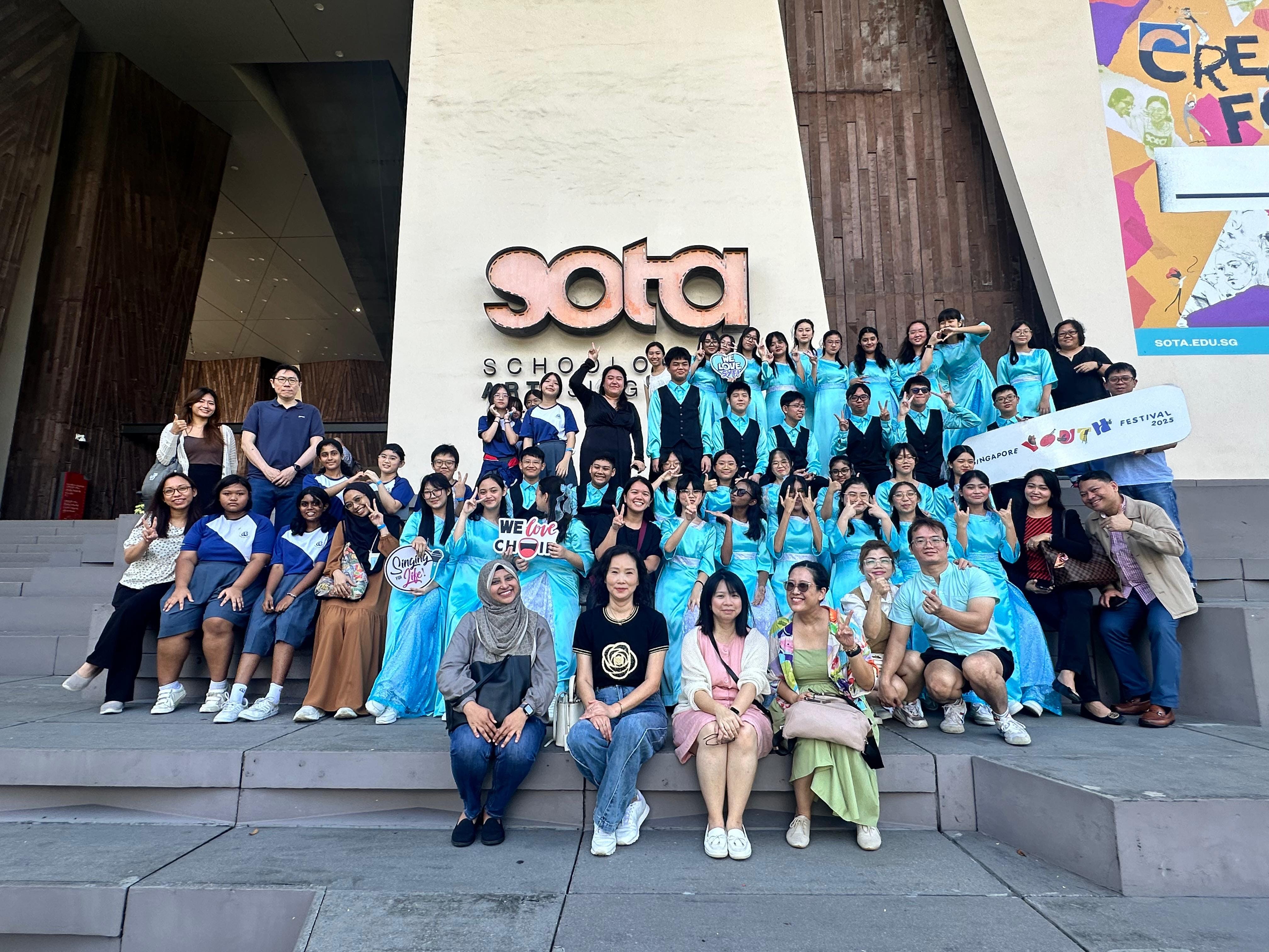 Large group of people in teal choir robes posing on steps outside the SOTA School of the Arts building.