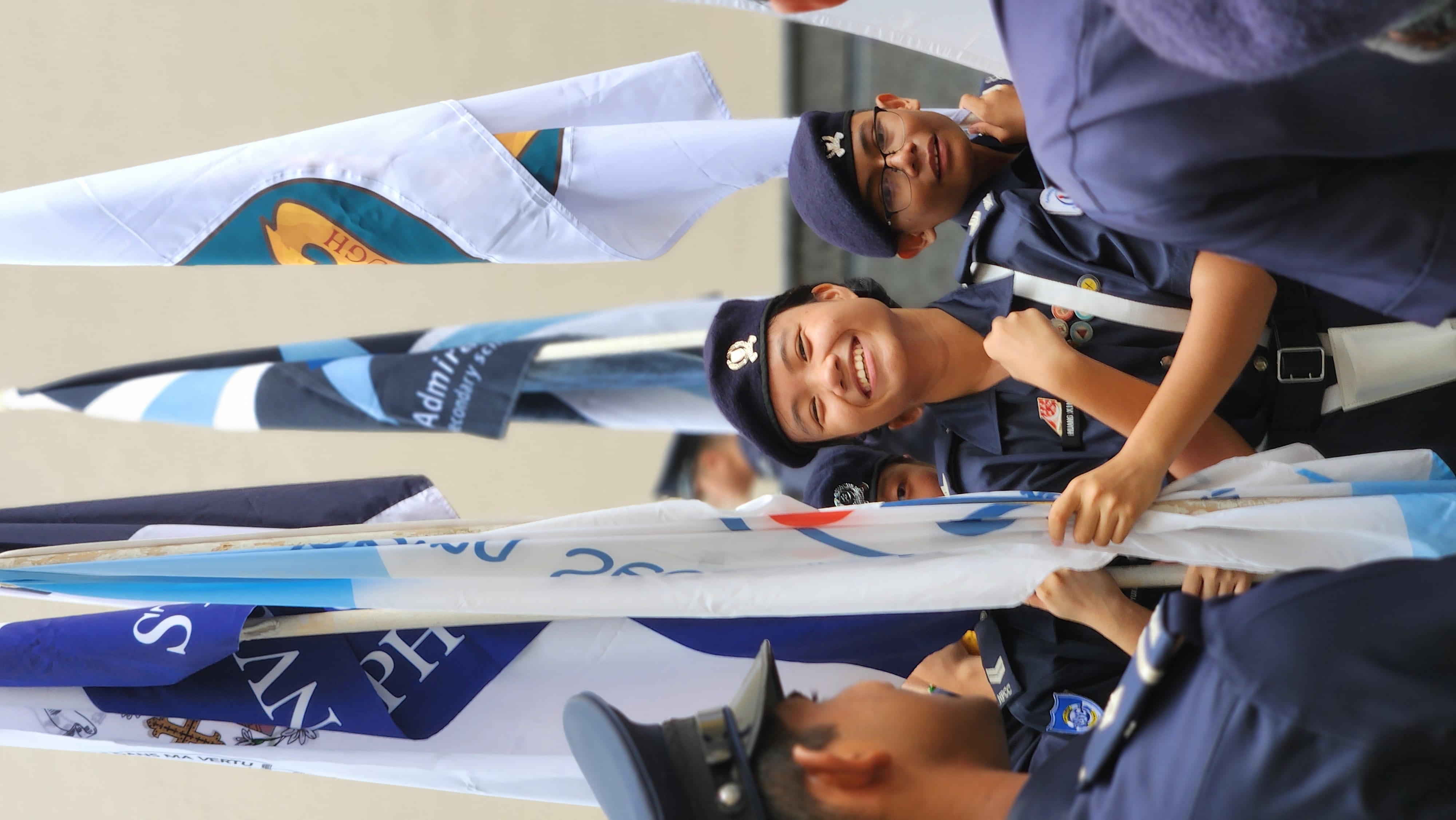 Uniformed cadets hold flags; one smiles at camera while others stand close behind.