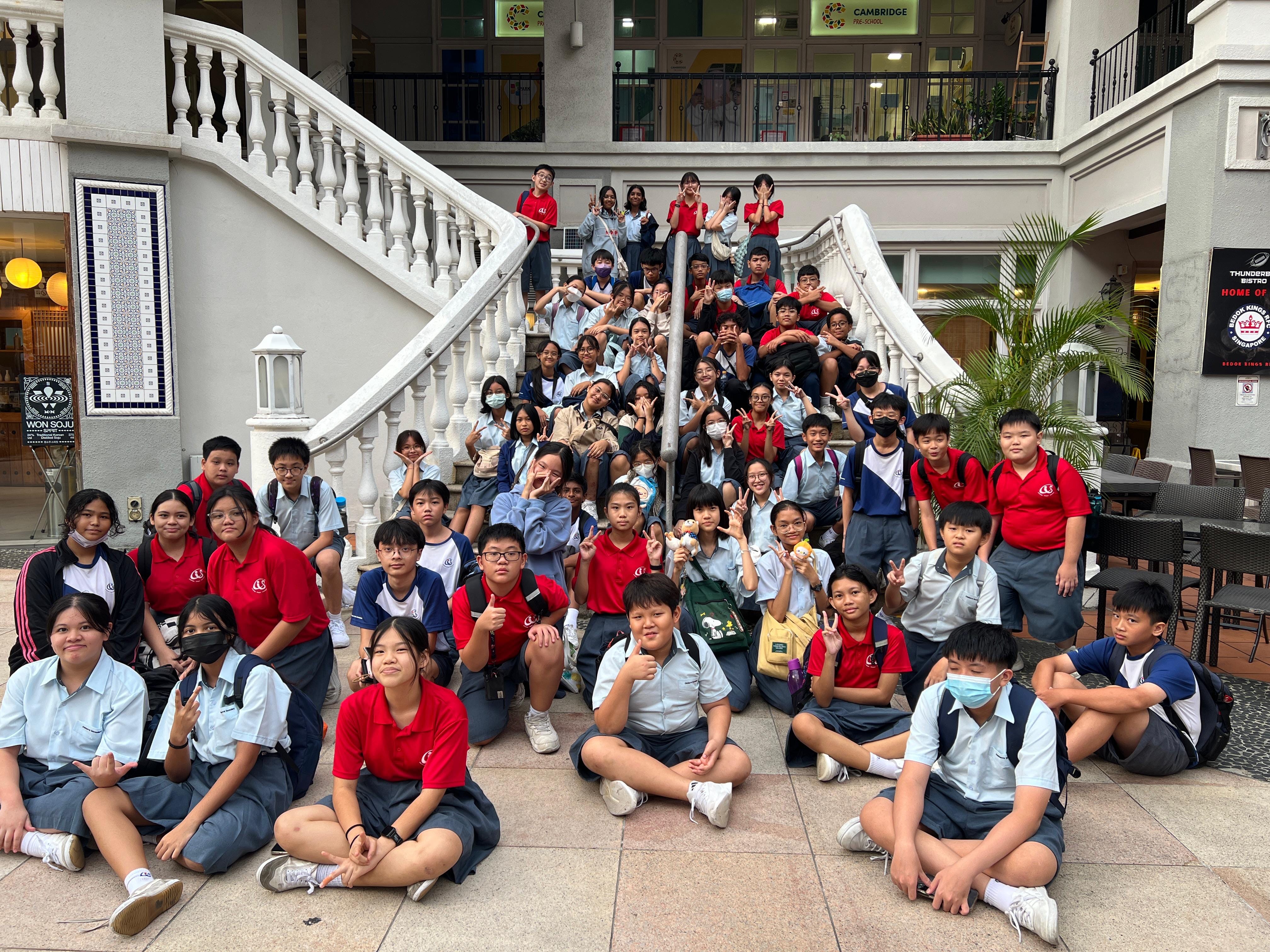 A large group of uniformed students posing on and around a white ornate staircase inside a building.
