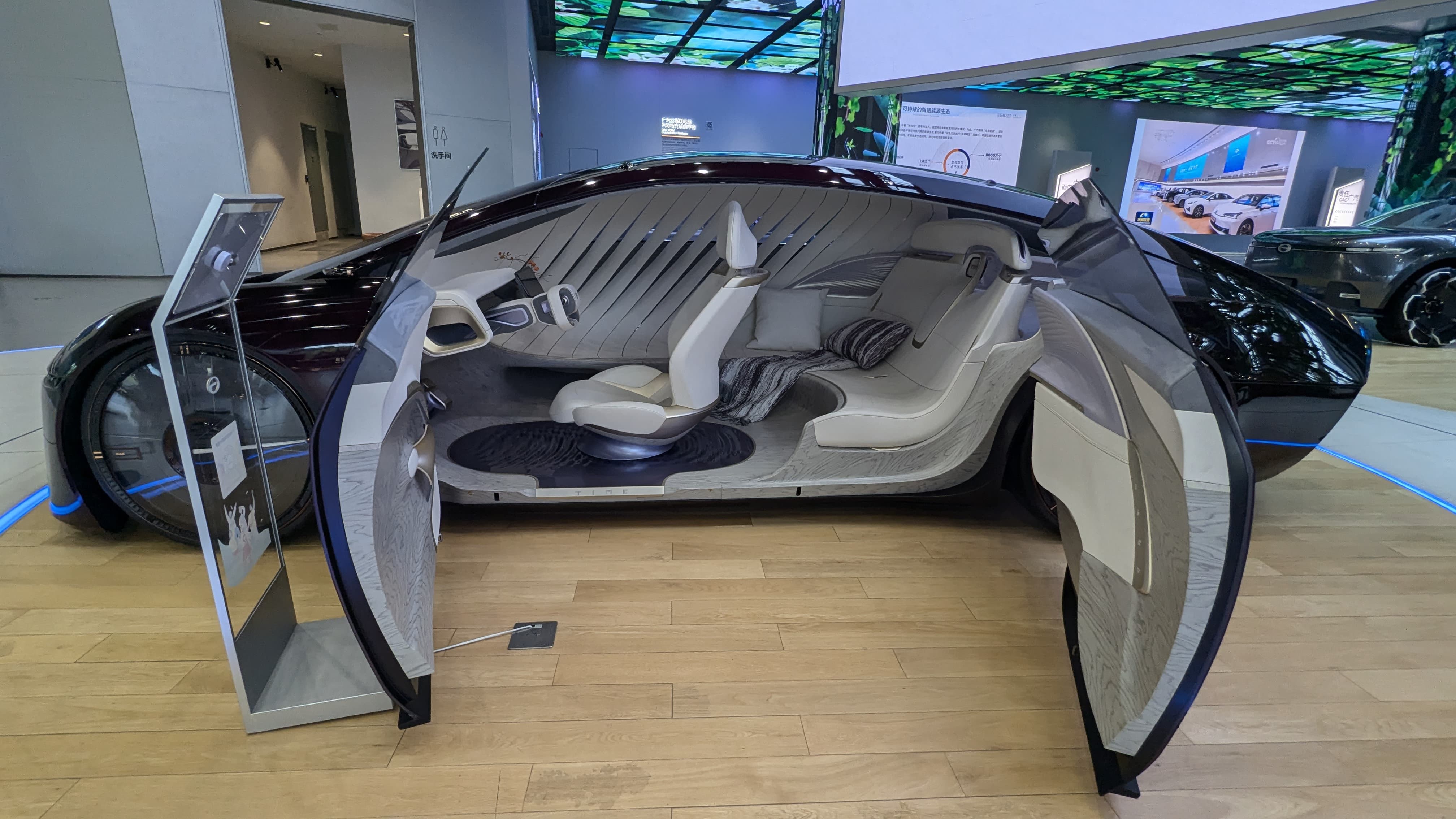 A futuristic concept car on display with open gull-wing doors revealing a luxury white interior with lounge seats.