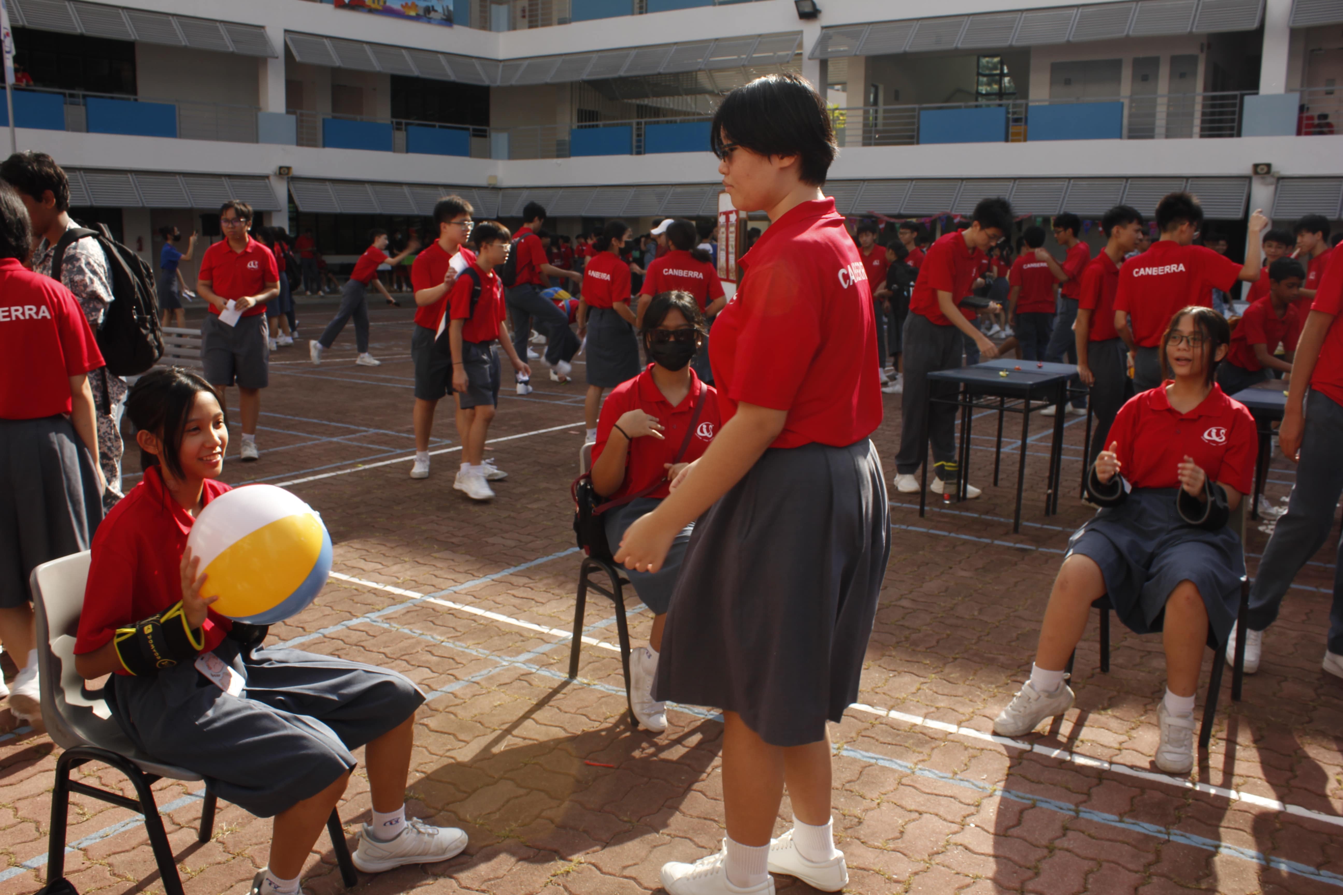 Students in red Canberra uniforms gather in an outdoor school courtyard, one holding a colorful beach ball.