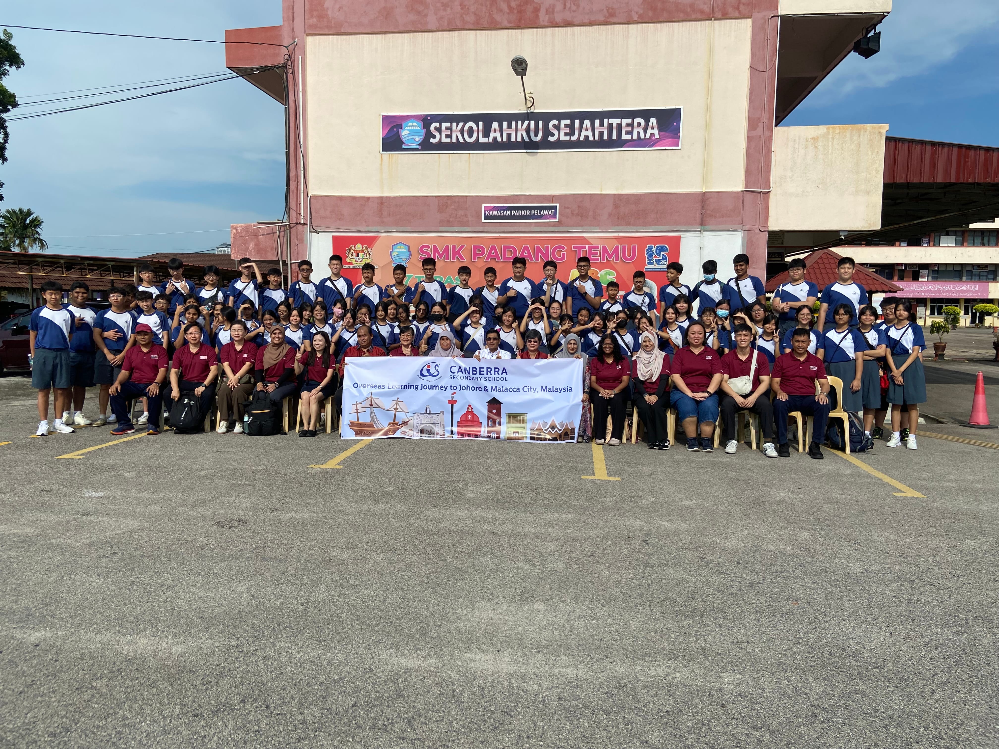 Large group of students and staff posing outside a school, holding a Canberra Secondary School banner.