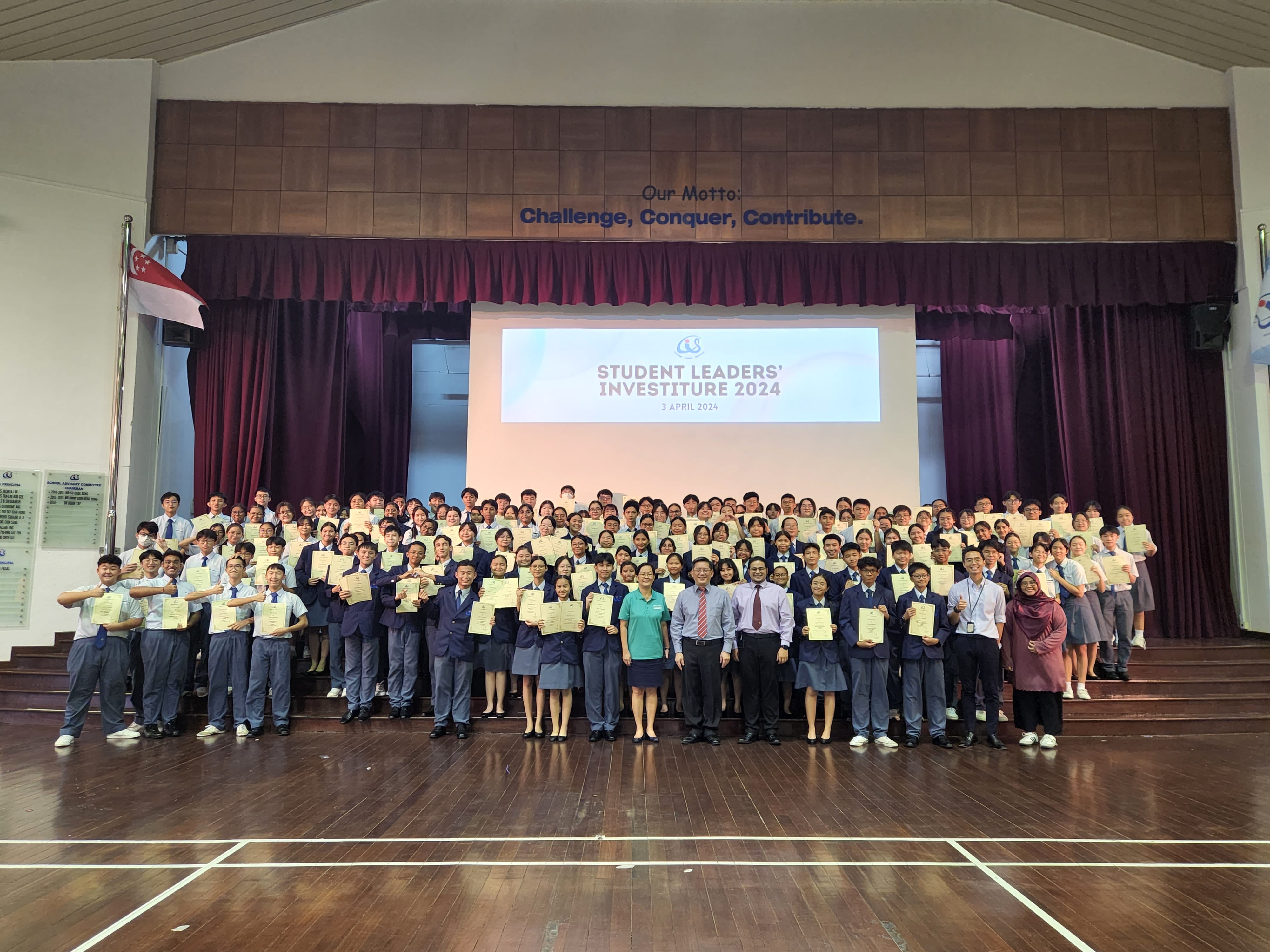 Large group of students holding certificates at a Student Leaders Investiture 2024 ceremony on April 3 in a school hall.