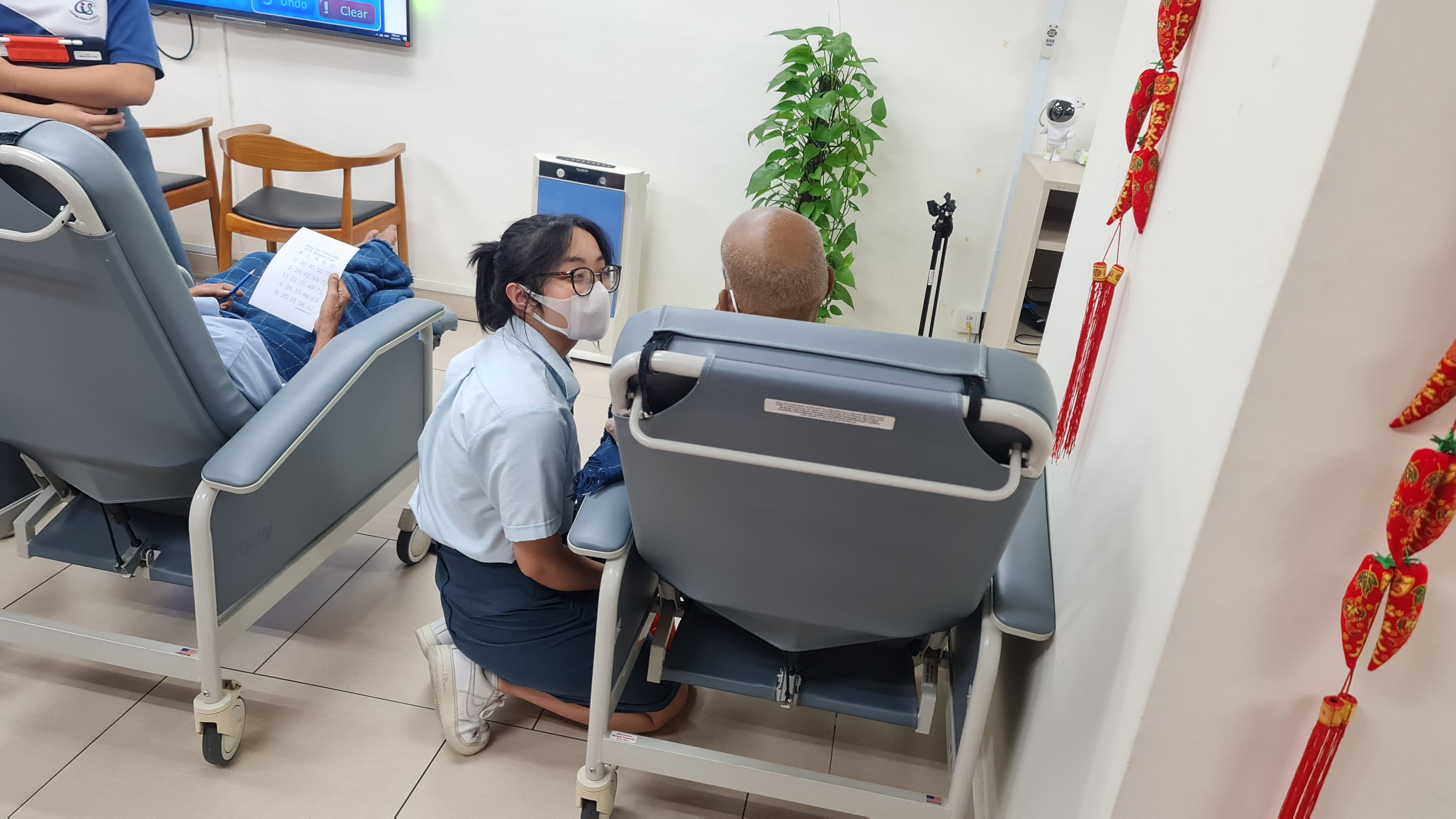 A student in school uniform speaks to an elderly man seated in a chair