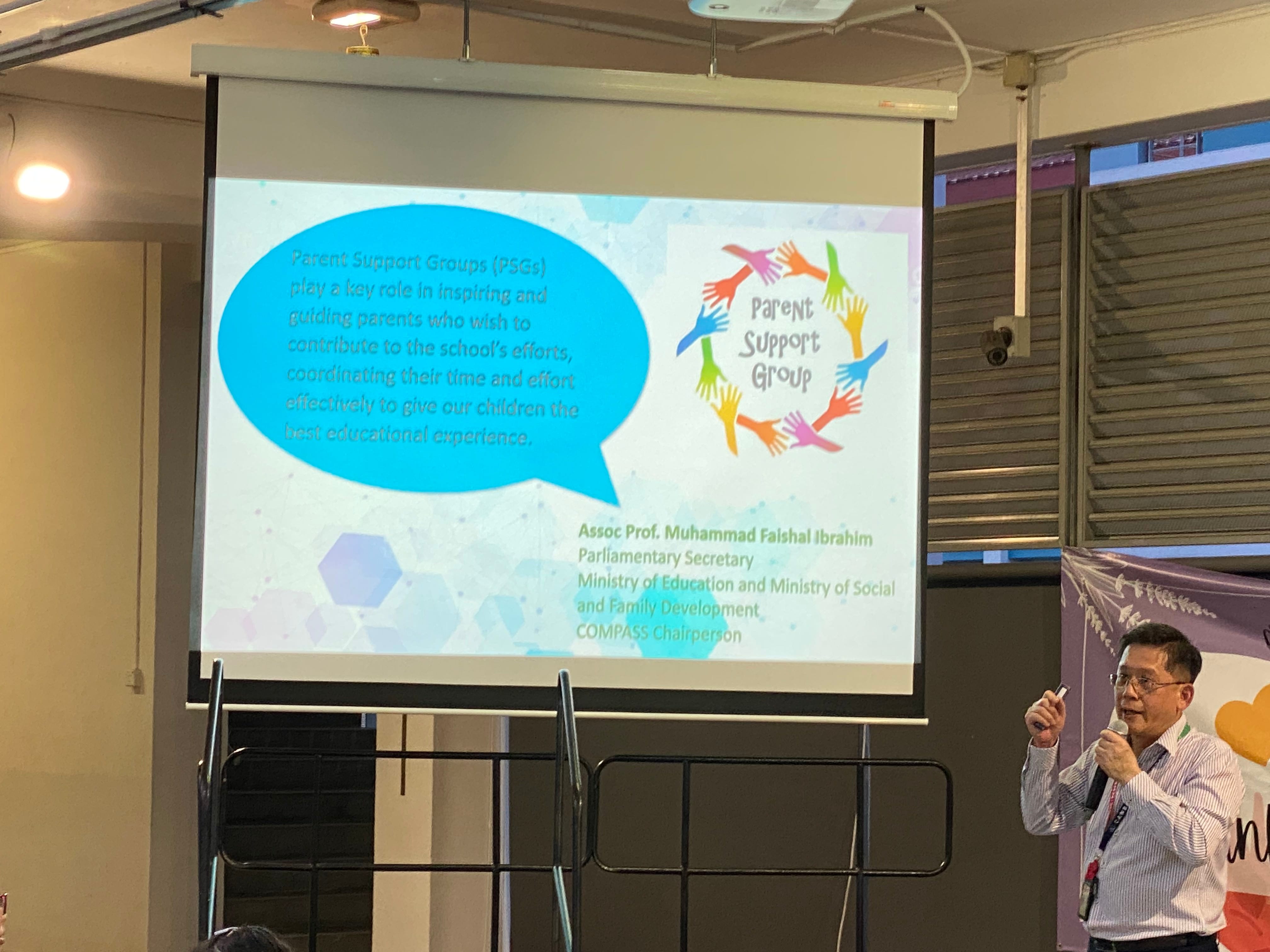 A man with a microphone presents beside a projected slide about Parent Support Groups with colorful hand icons.
