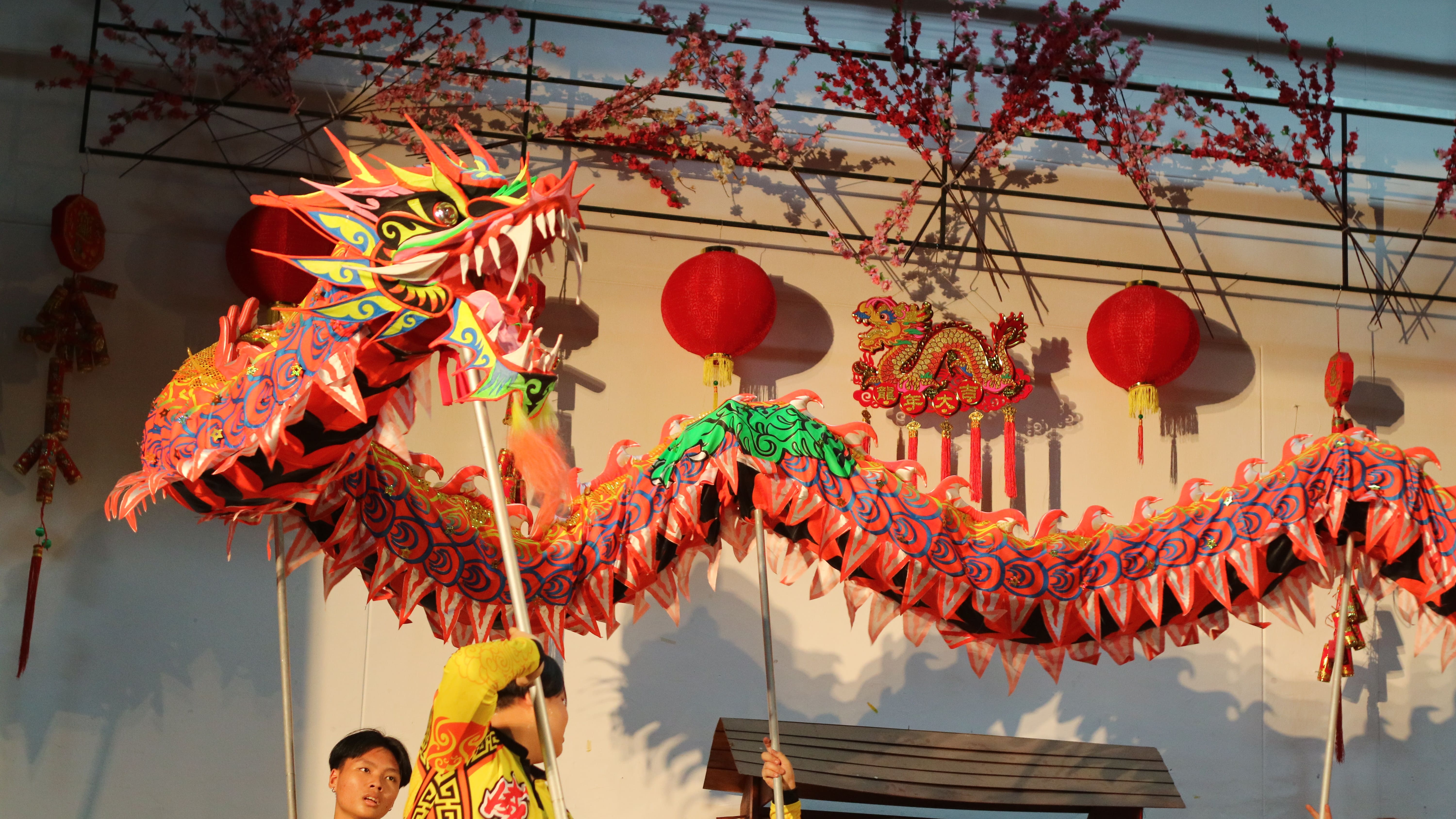 Performers in yellow costumes hold poles lifting a colorful red dragon costume during a Chinese dragon dance celebration.