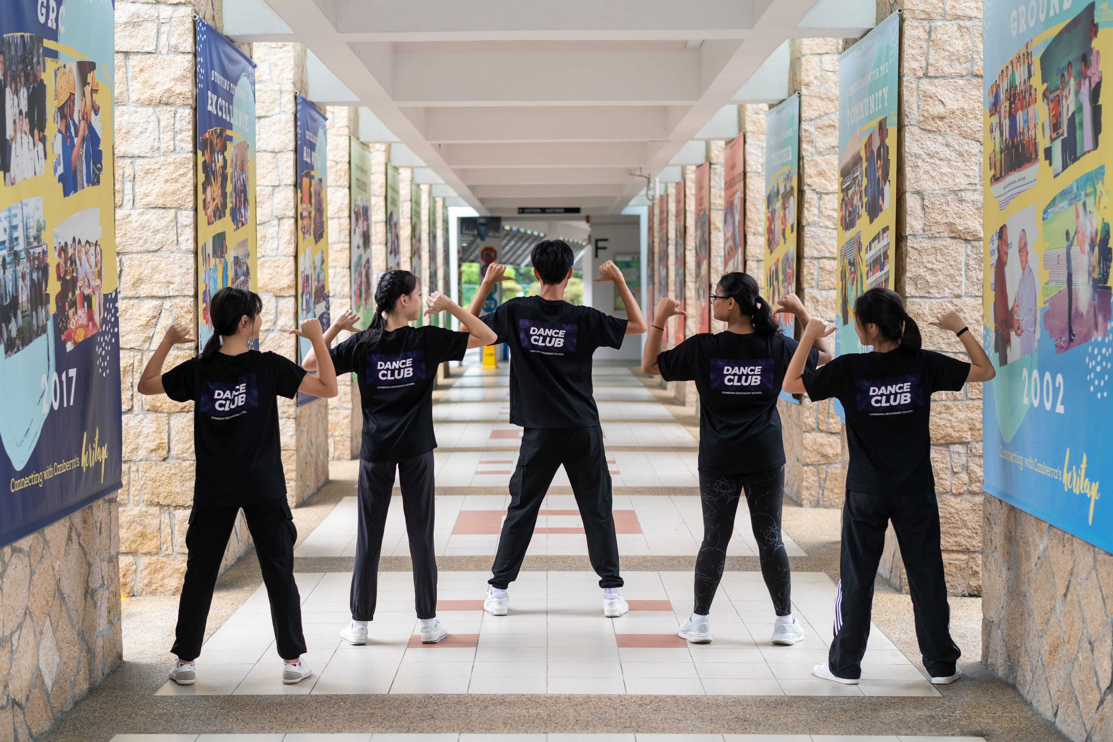 Students in black tees, with their back to the camera point to the text on the back of their tees