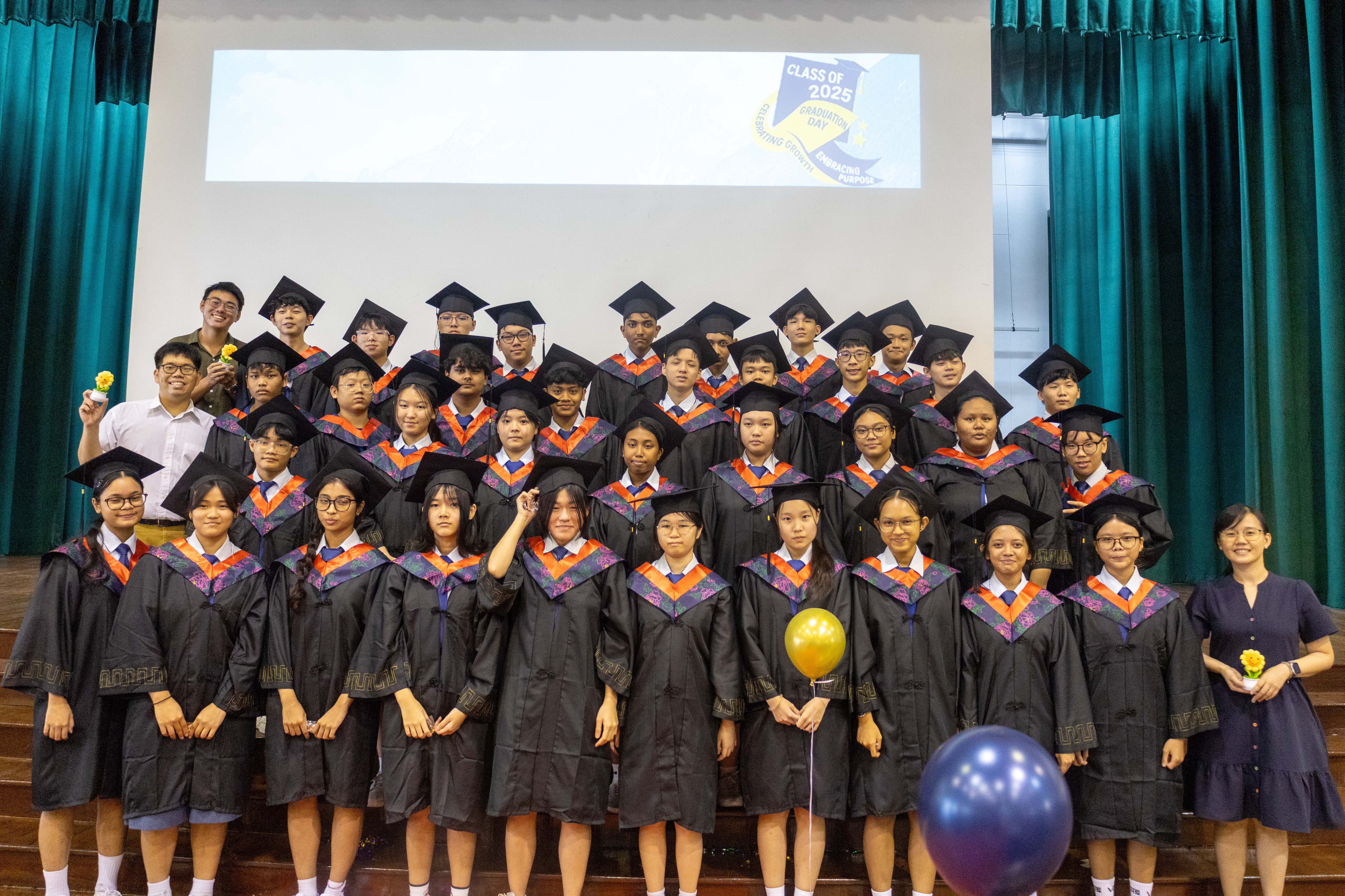 Large group of students in black graduation gowns and caps pose on a stage for Class of 2025 Graduation Day.