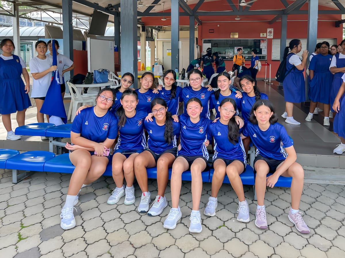 A group of young girls in matching blue sports uniforms posing together on blue benches at a school.