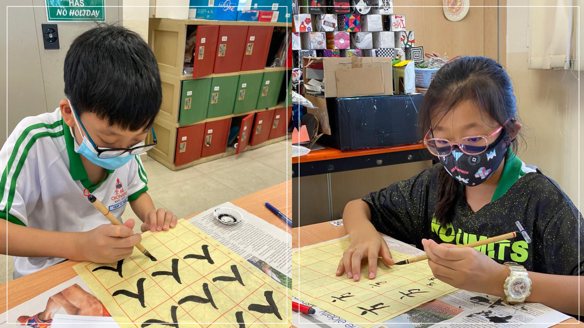 Two masked children practice Chinese calligraphy with brushes on yellow grid paper in a classroom.