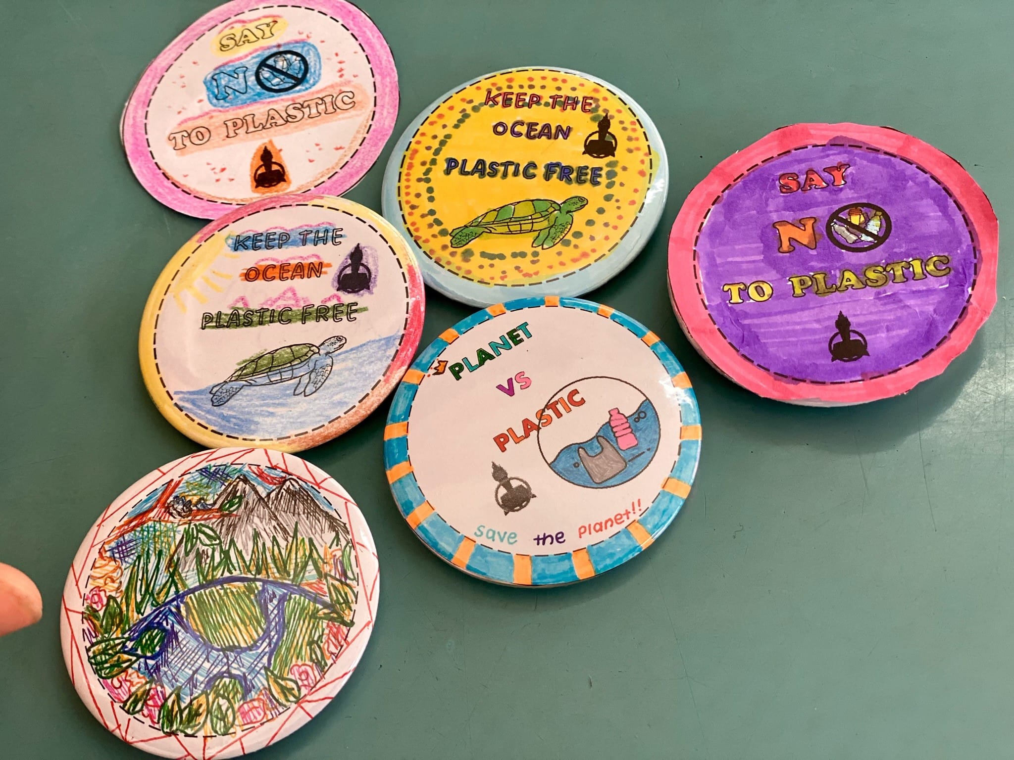 Six hand-drawn circular badges with anti-plastic slogans like "Say No To Plastic" and "Keep The Ocean Plastic Free."