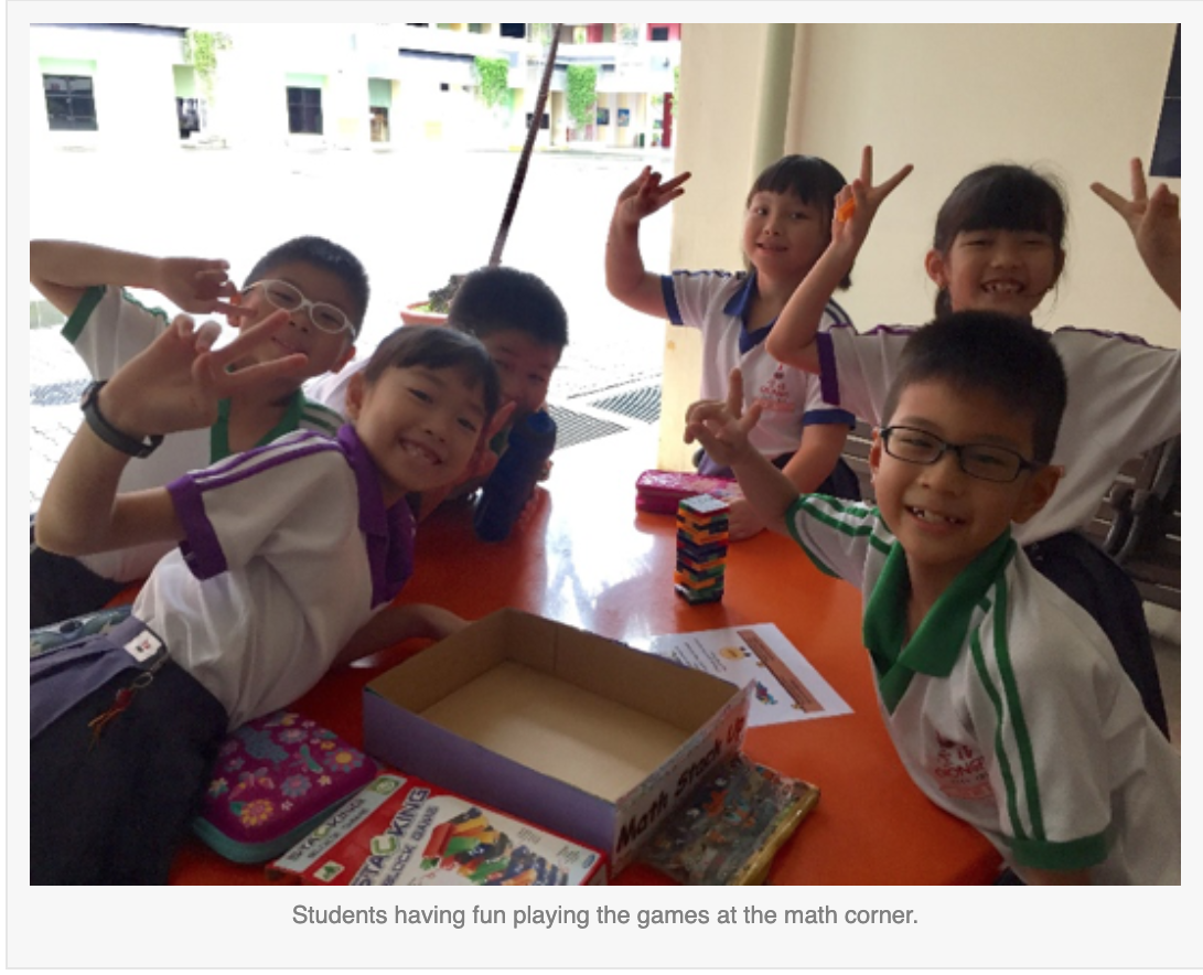 Six young students in school uniforms smile and pose with peace signs around an orange table with board games.