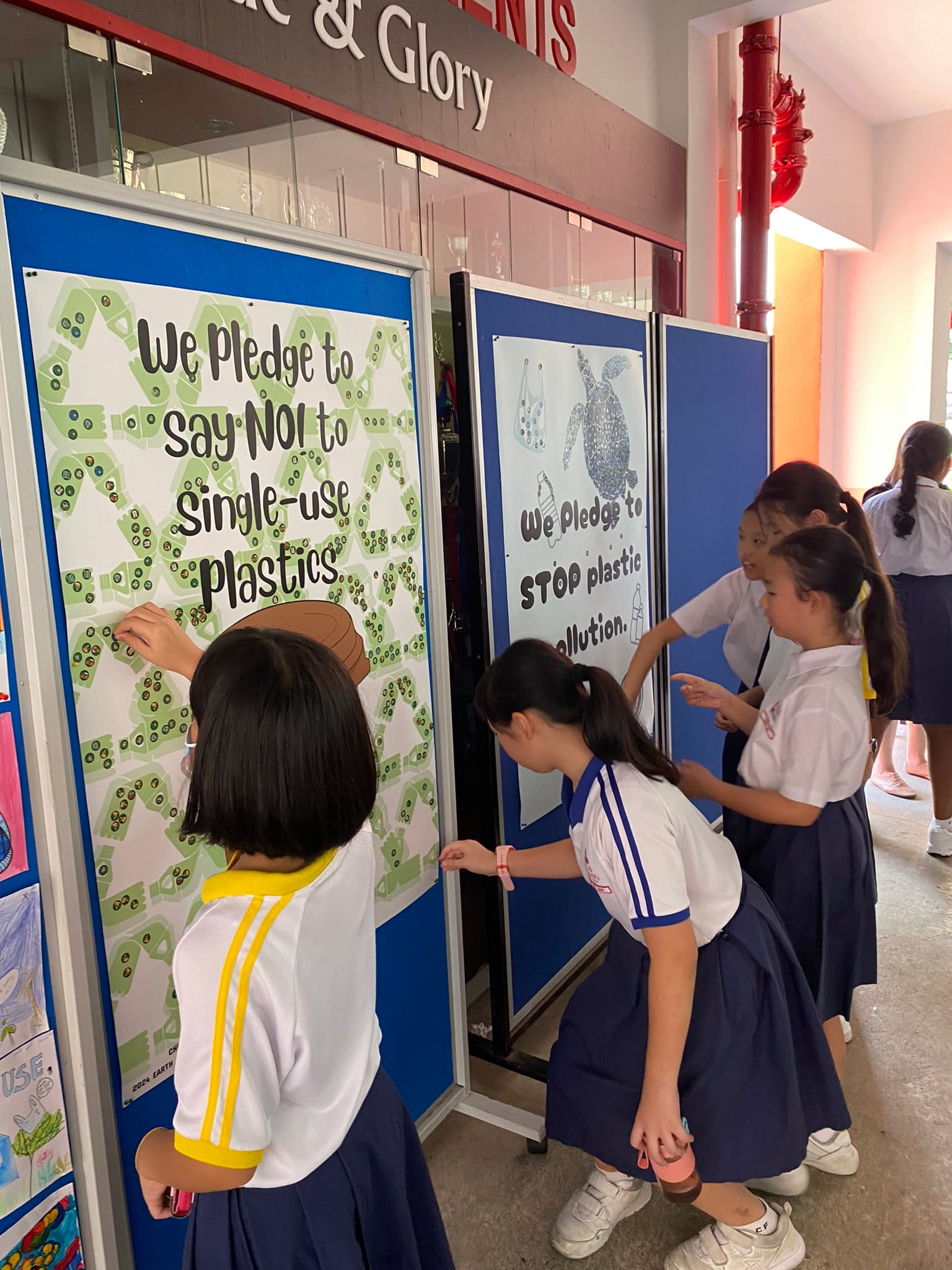 Young students in uniforms adding stickers to pledge boards about saying no to single-use plastics.