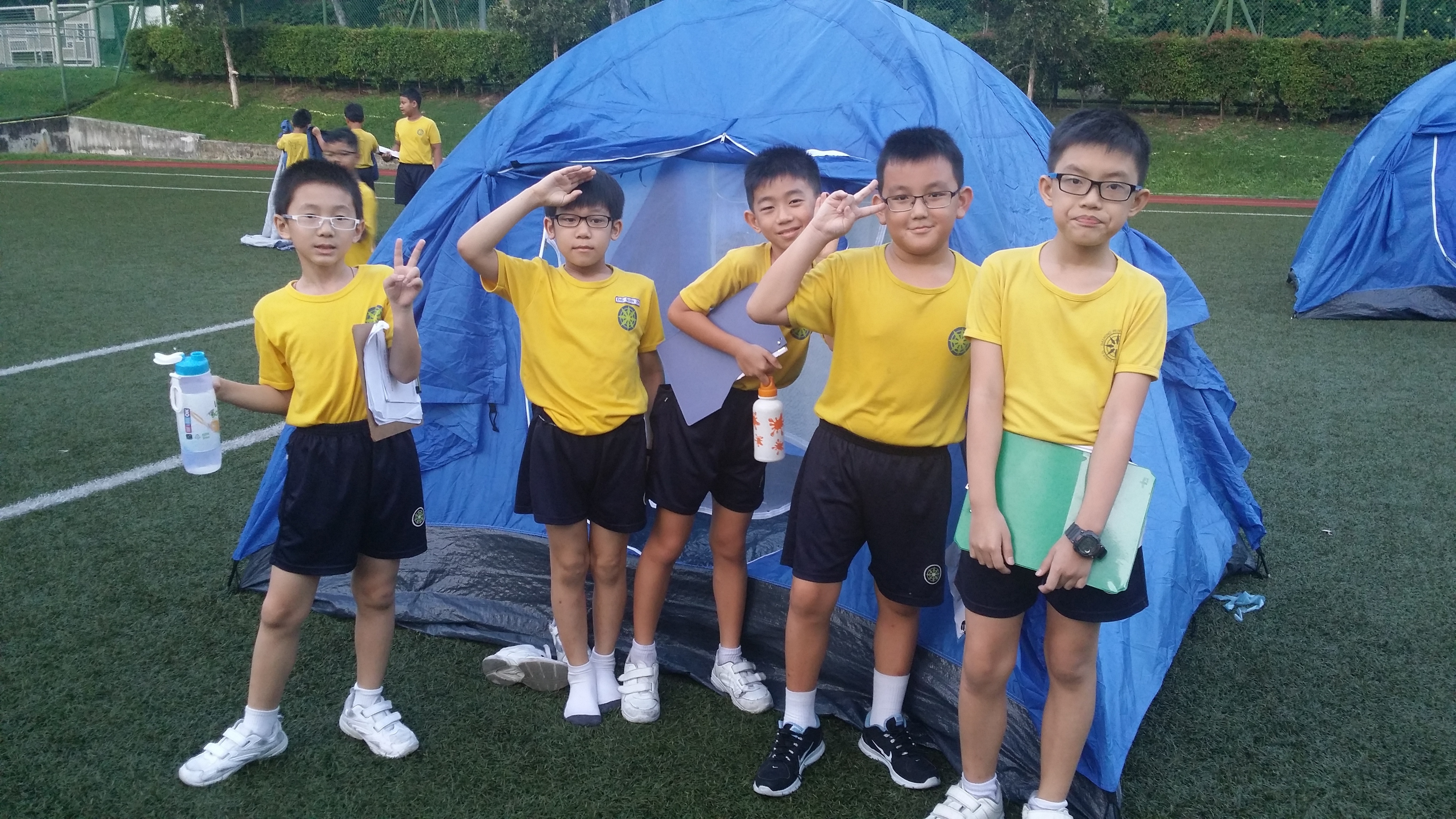 Five boys in yellow uniforms pose in front of a blue dome tent on a grass field.