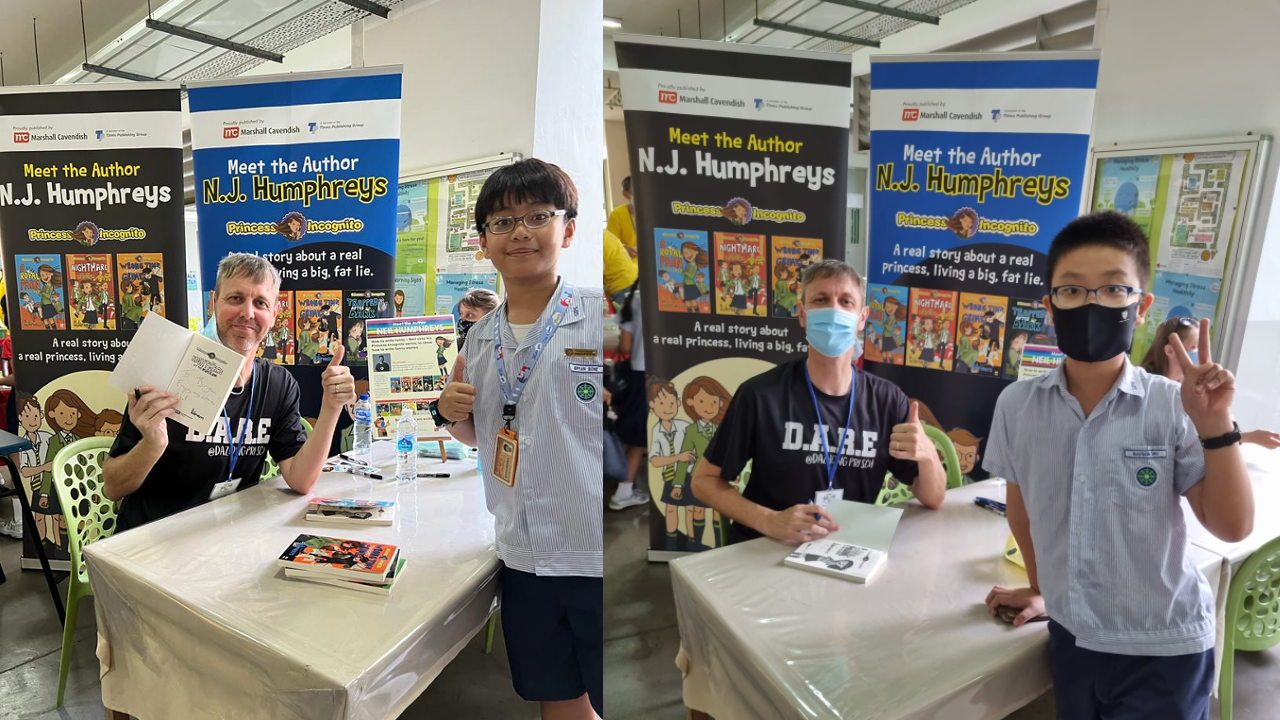 Author N.J. Humphreys sits at a signing table posing with two young students in front of Meet the Author banners.