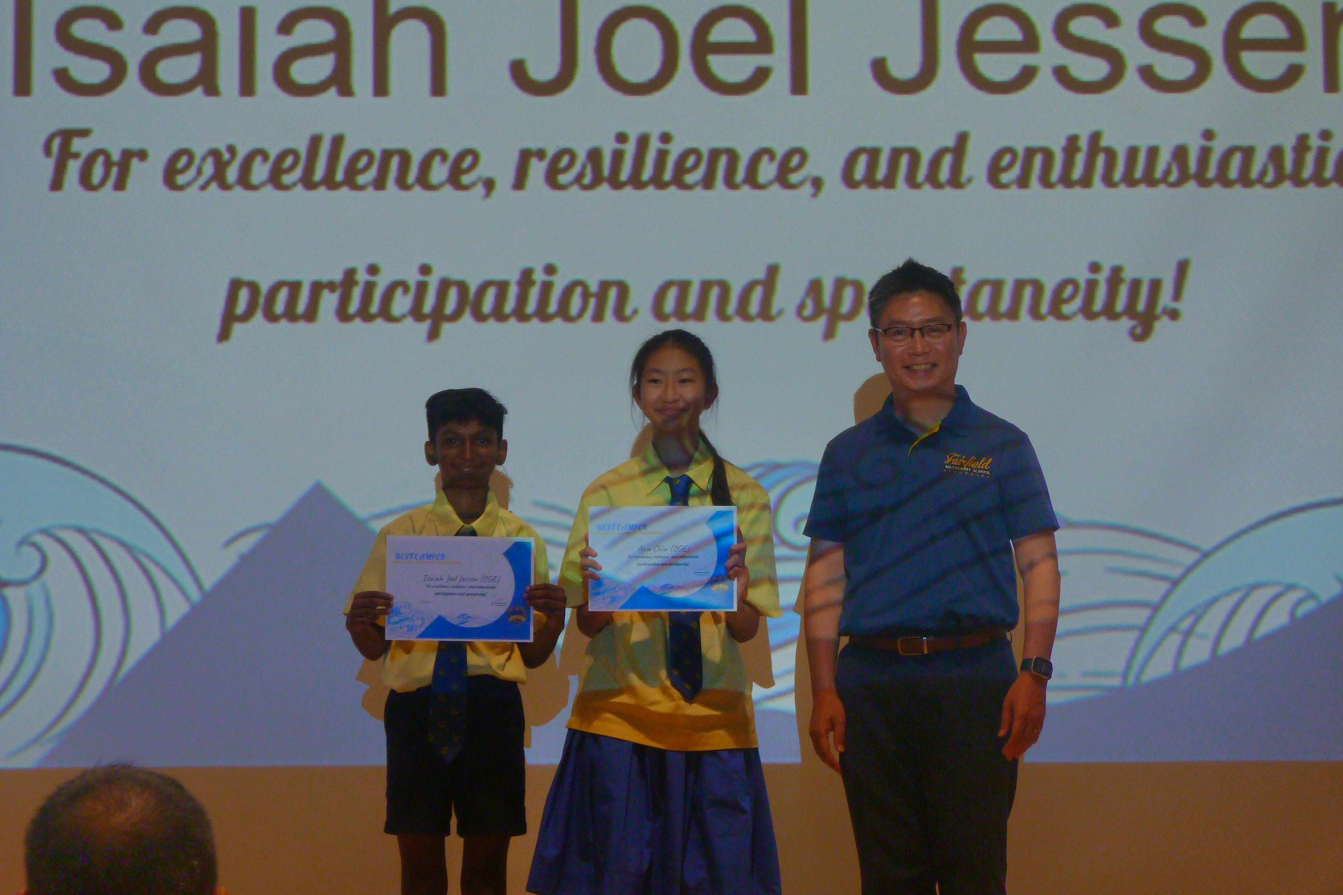 Principal Mr. Wee Tat Chuen standing proudly alongside two Secondary One award recipients holding their certificates on stage during the Installation Night ceremony.