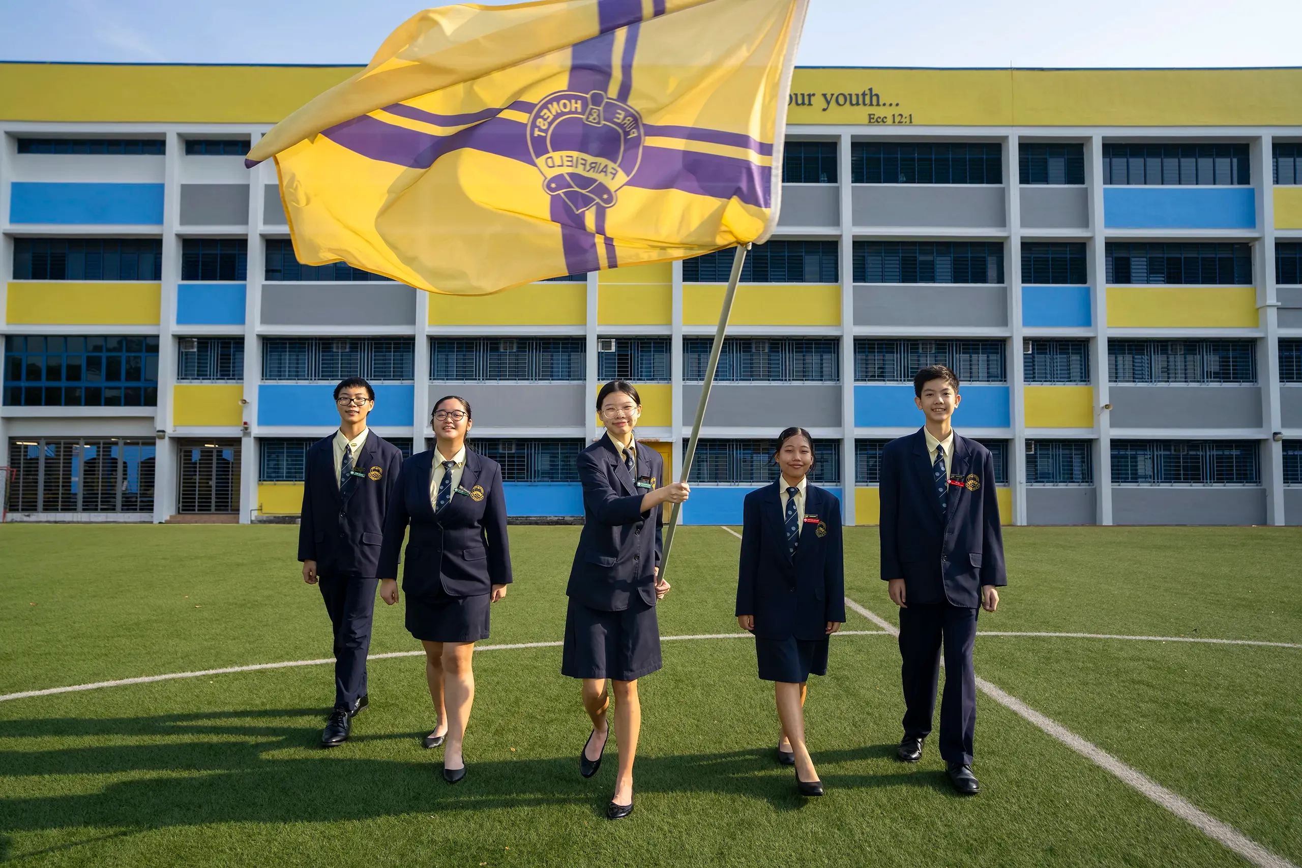 Five students in navy blazers walking on the field as one holds a Fairfield Flag.