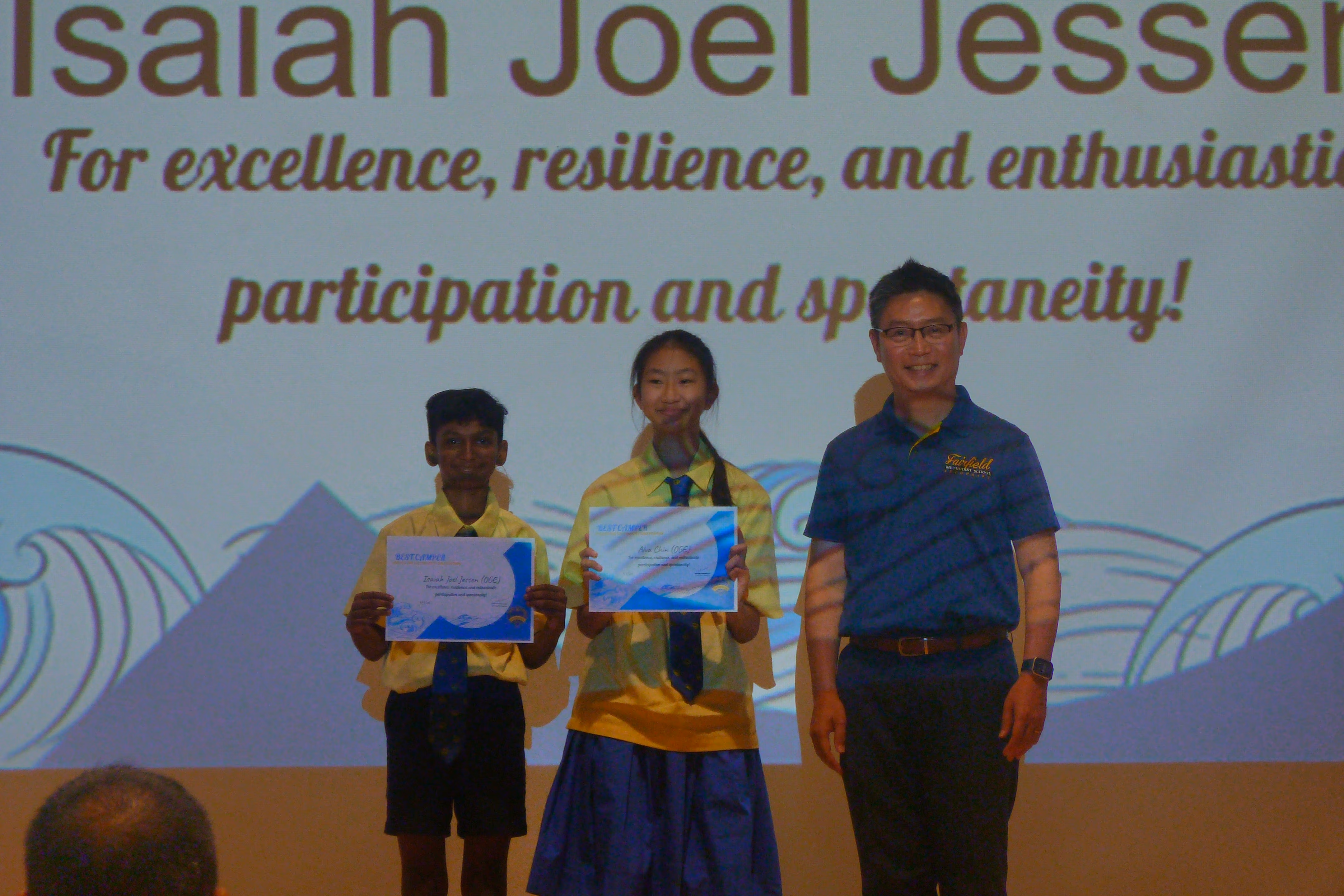 Principal Mr. Wee Tat Chuen smiling alongside two Secondary One student award recipients holding their certificates on stage during the Secondary One Orientation.