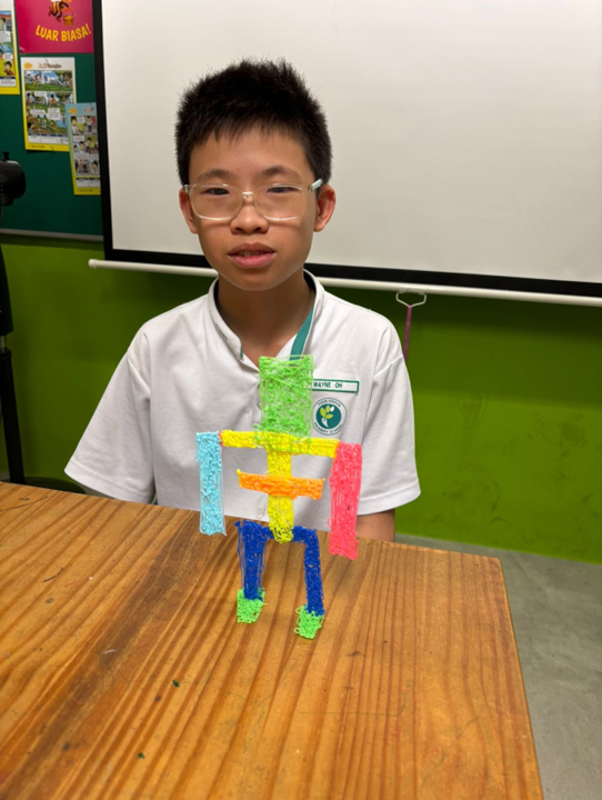 A young boy in a school uniform and glasses sits behind a desk displaying a colorful 3D-pen figure of a human shape.