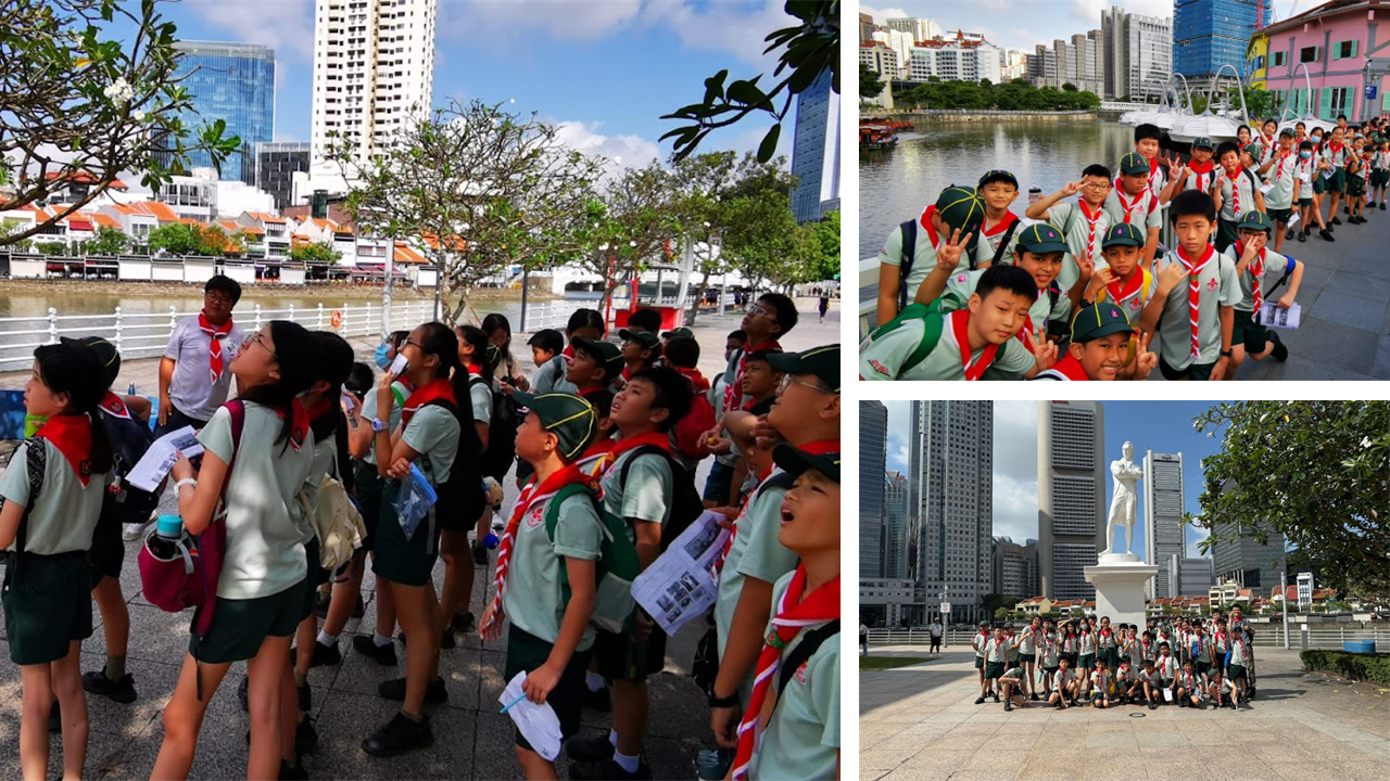 Students in scout uniforms with red scarves on an outdoor field trip near a river and a white statue in a city.