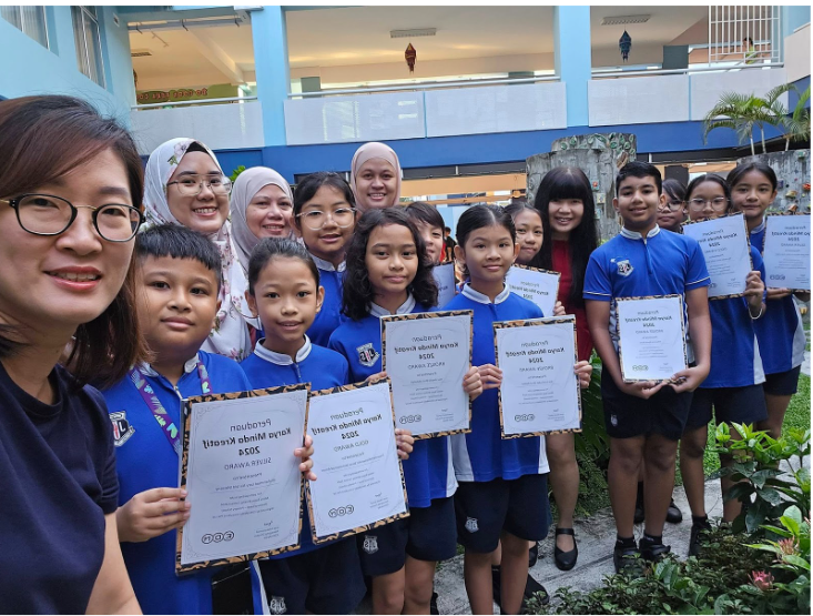 Group of students in blue uniforms holding certificates, posing with teachers outdoors at a school.