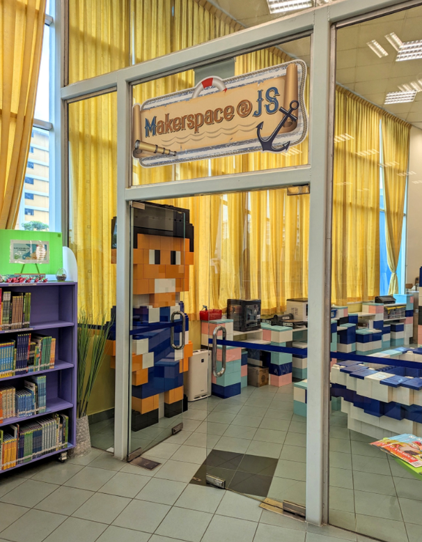 Entrance to a room labeled Makerspace at JS with a pixel-art character on the glass door and a purple bookshelf nearby.