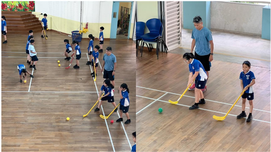 Children in blue uniforms practice floor hockey with yellow sticks indoors, supervised by an adult coach.
