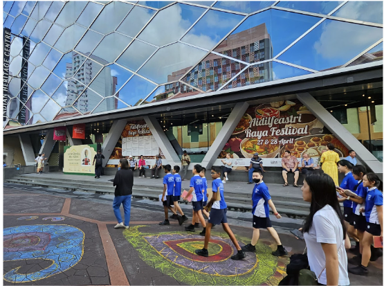 Students in blue uniforms walk past a modern glass building with a Aidil Feastri Raya Festival banner on April 27 and 28.