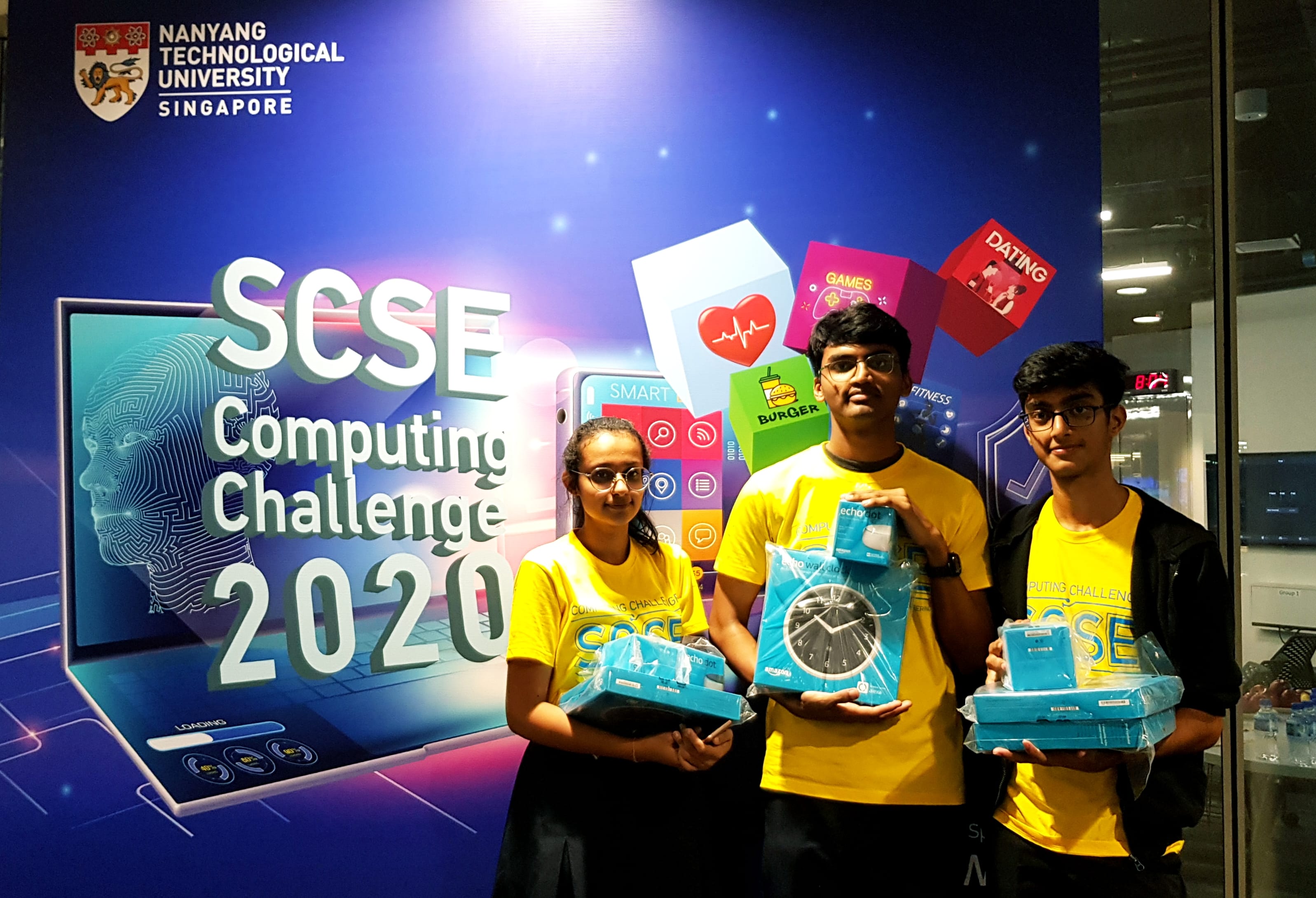 Three students in yellow shirts hold prizes in front of SCSE Computing Challenge 2020 banner at NTU Singapore.