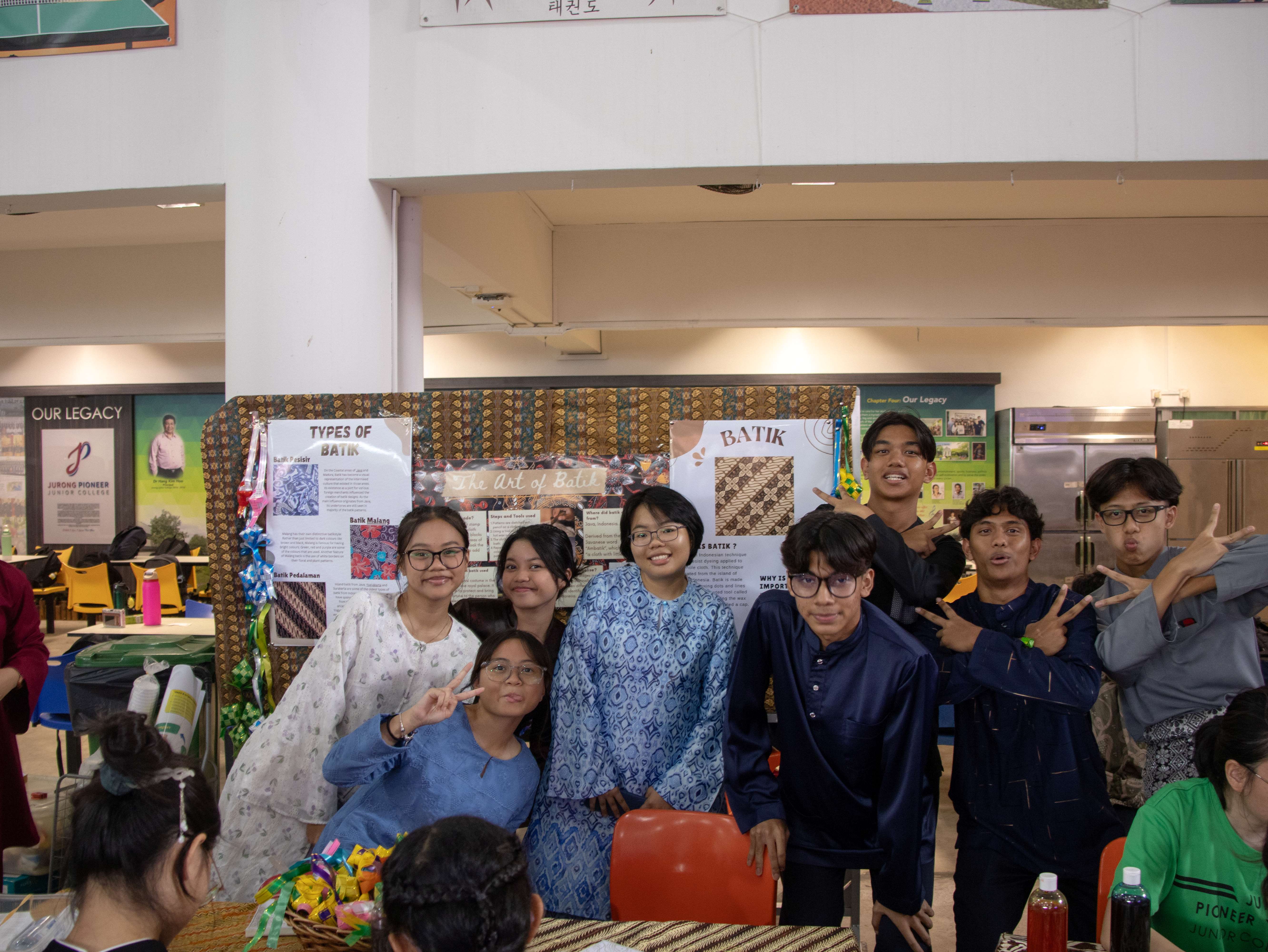 Students in traditional attire pose in front of a Batik display board at Jurong Pioneer Junior College.