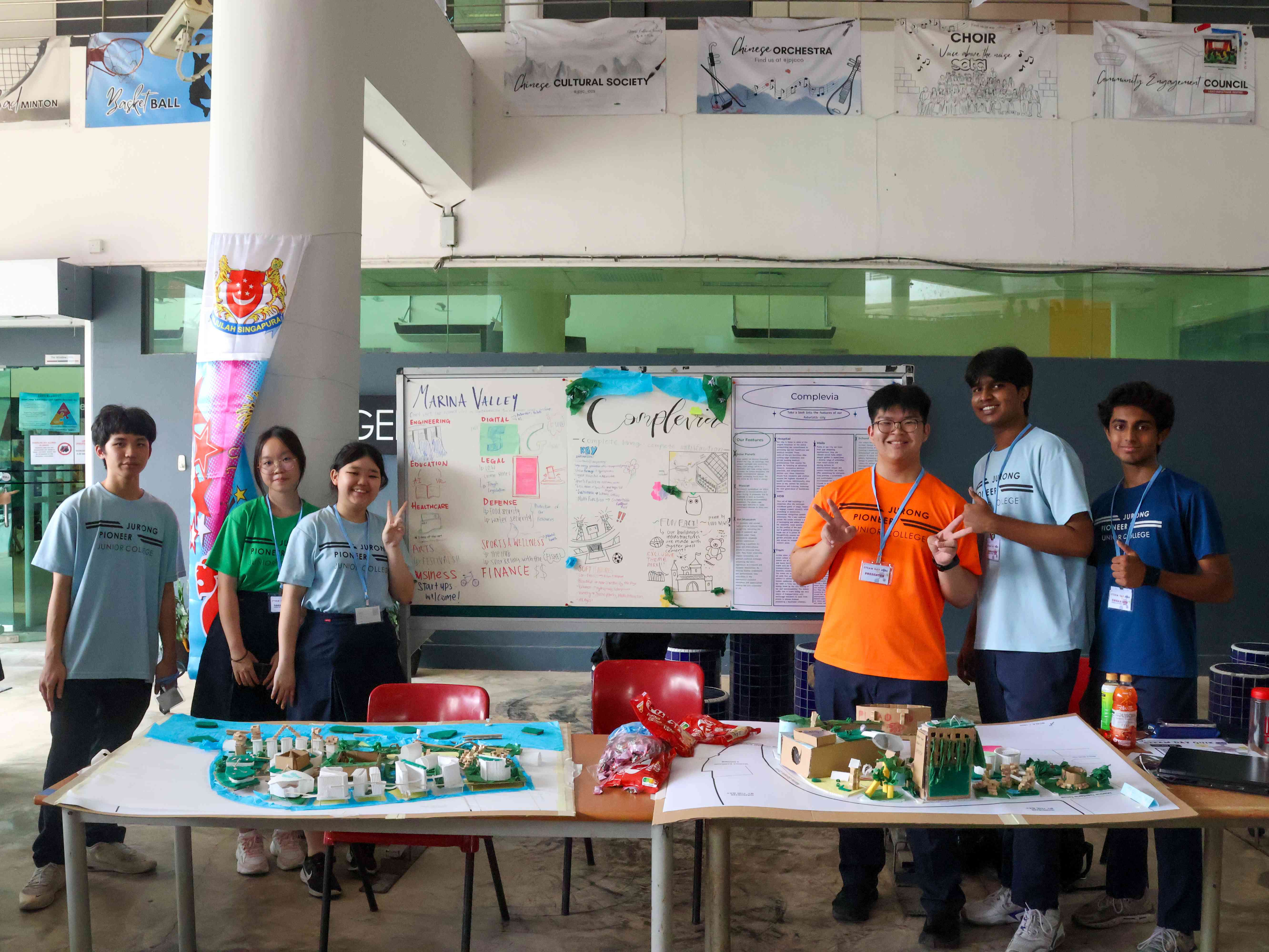 Six students stand behind tables displaying city planning models and project boards at a school fair.