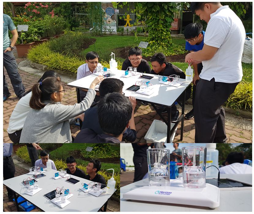 Students gathered around an outdoor table conducting a science experiment with Horizon fuel cell kits and water containers.